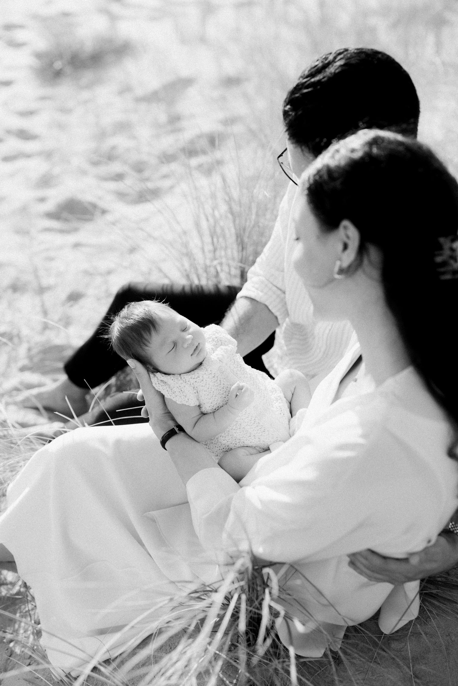 Black and white portraits of family bonding with baby in natural outdoor setting.