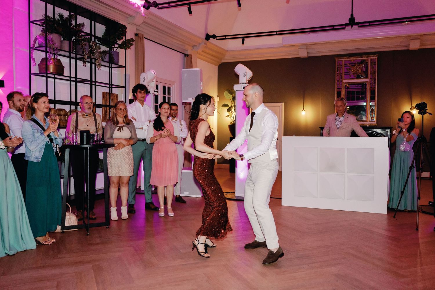 Dancers perform an elegant spin on a wooden dance floor at a wedding reception with pink and purple lighting.