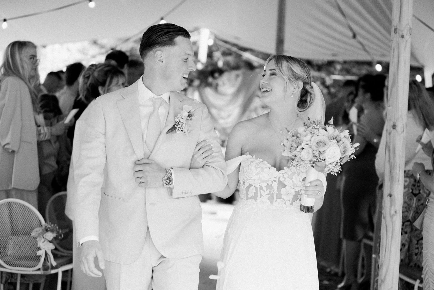 Wedding guests dancing and celebrating under a white tent at an outdoor reception.