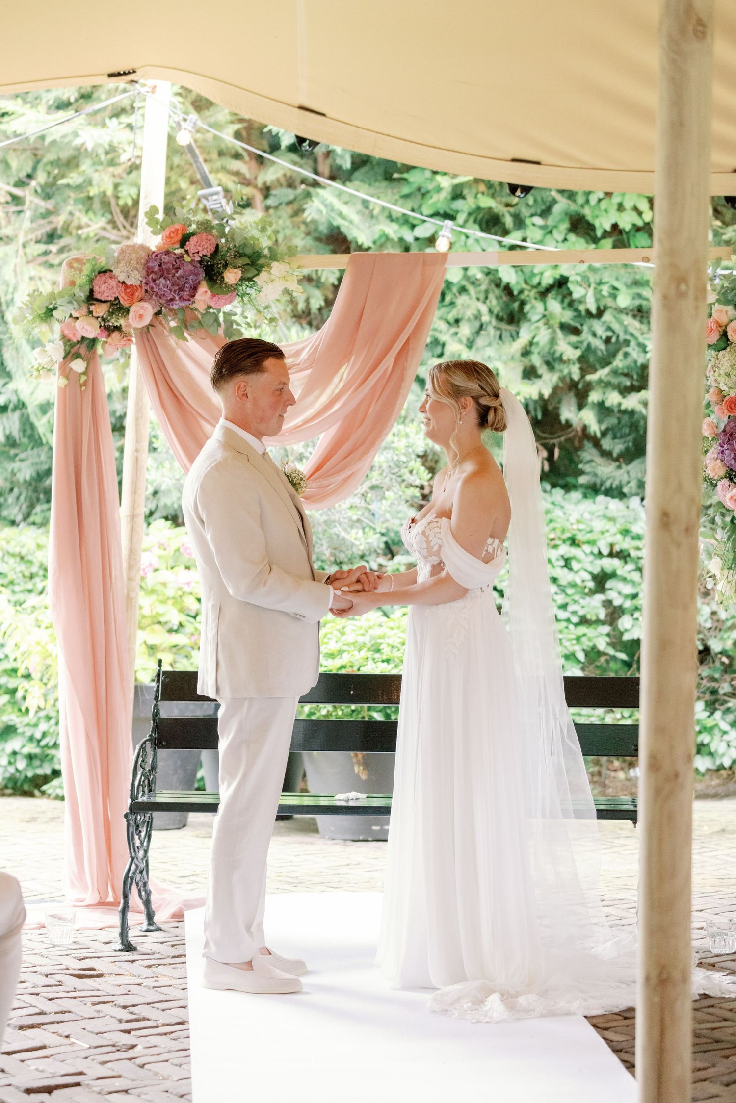 A couple shares a romantic dance under a covered outdoor pavilion decorated with soft pink drapes.