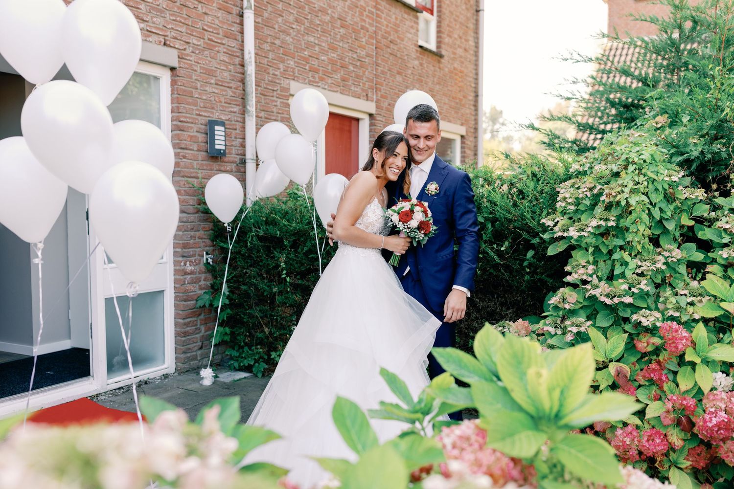 Wedding couple posing with white balloons outside a brick building on their special day.