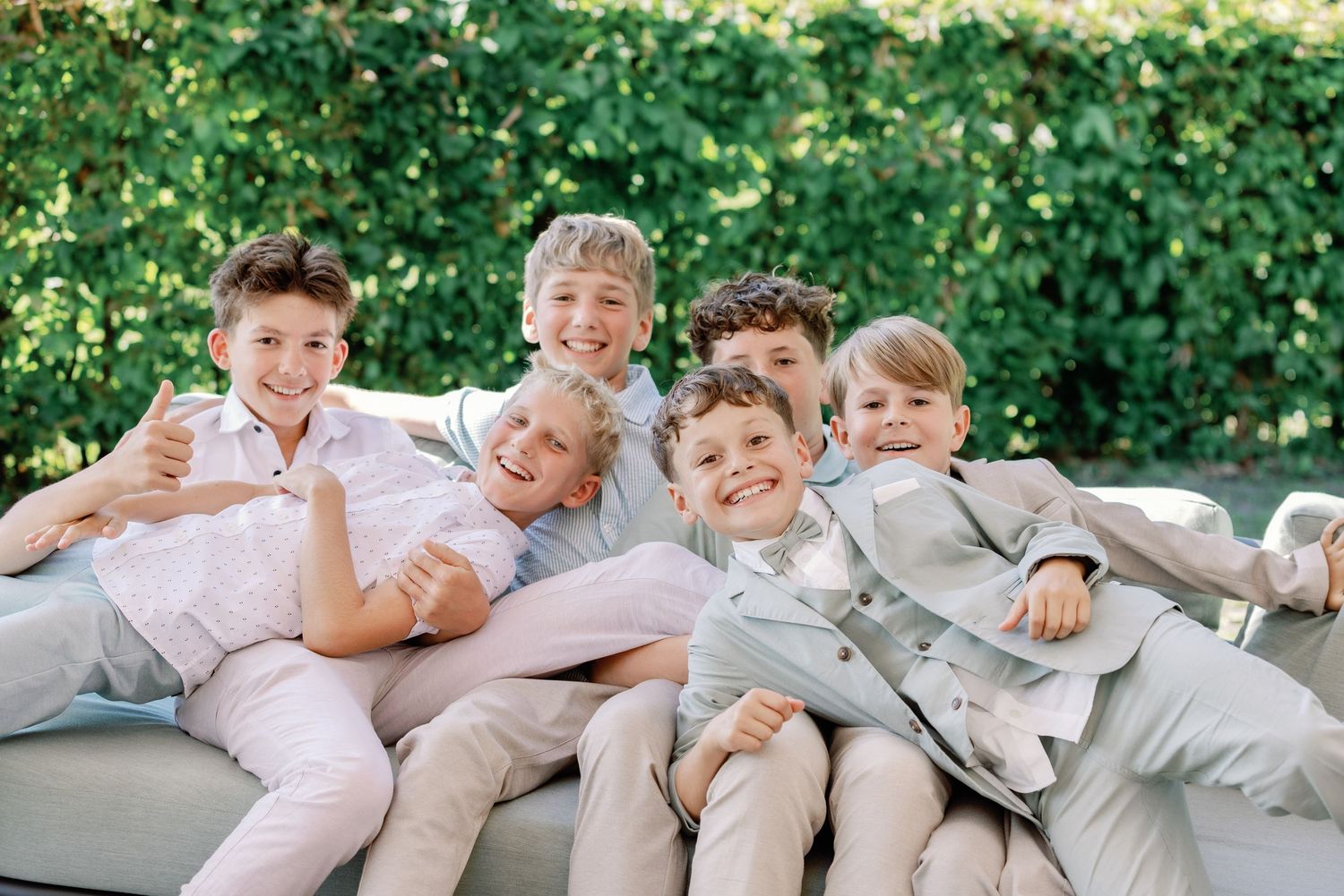 A group in coordinated beige and white outfits poses playfully on concrete steps outdoors with greenery in background.