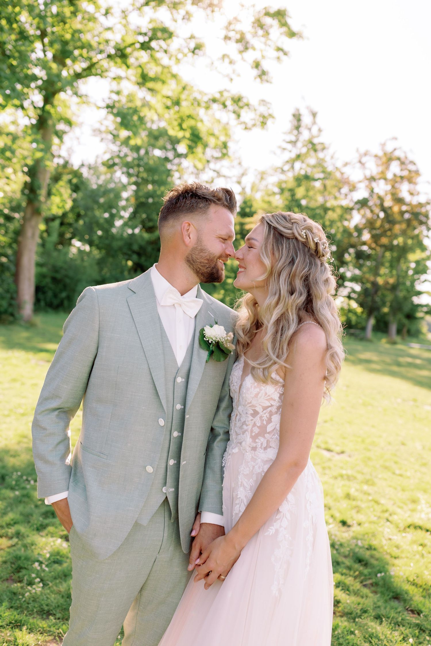 A romantic wedding couple shares tender moments in a sun-drenched garden setting wearing light colored attire.