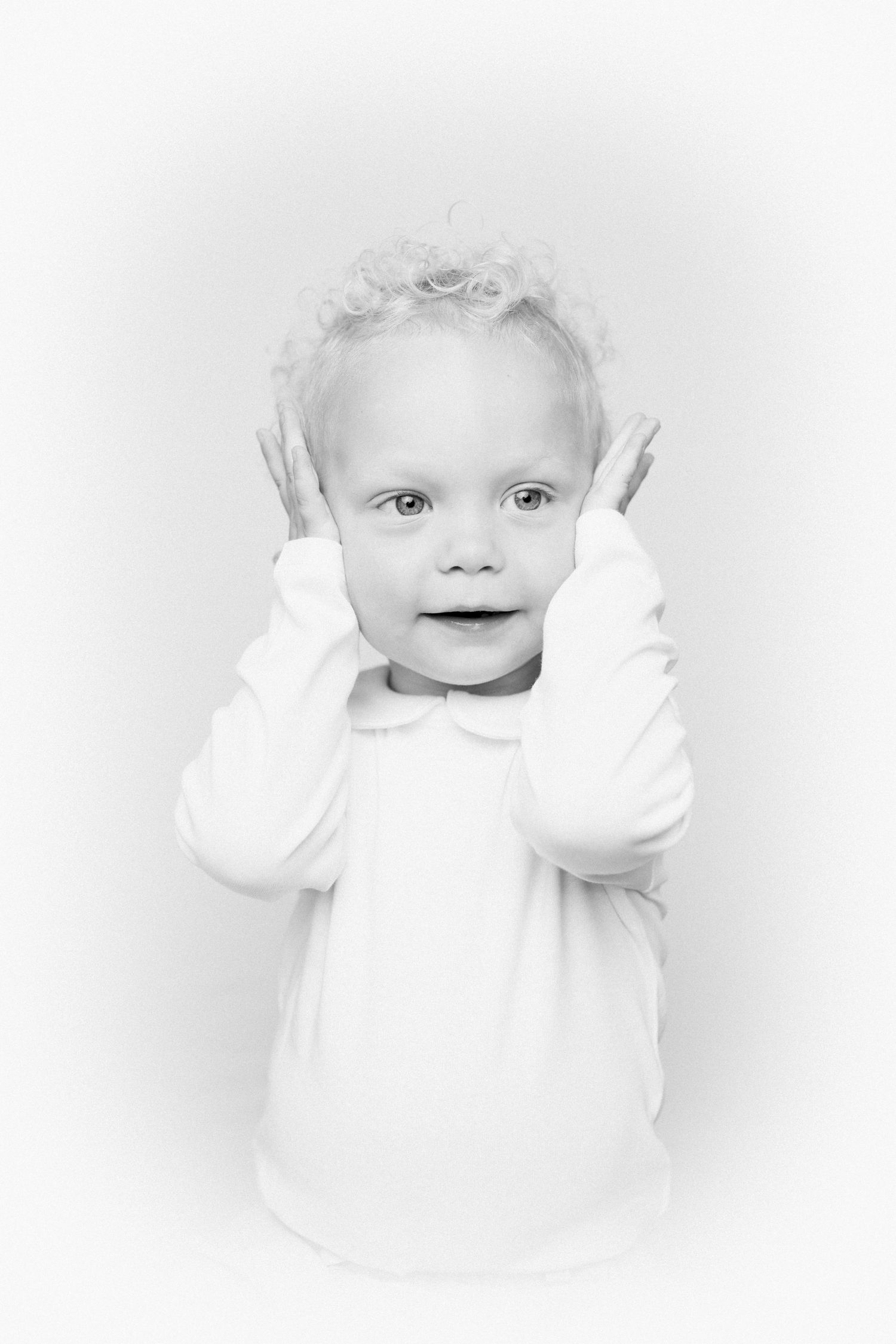 Sweet candid moments of a baby in white clothing against light background.