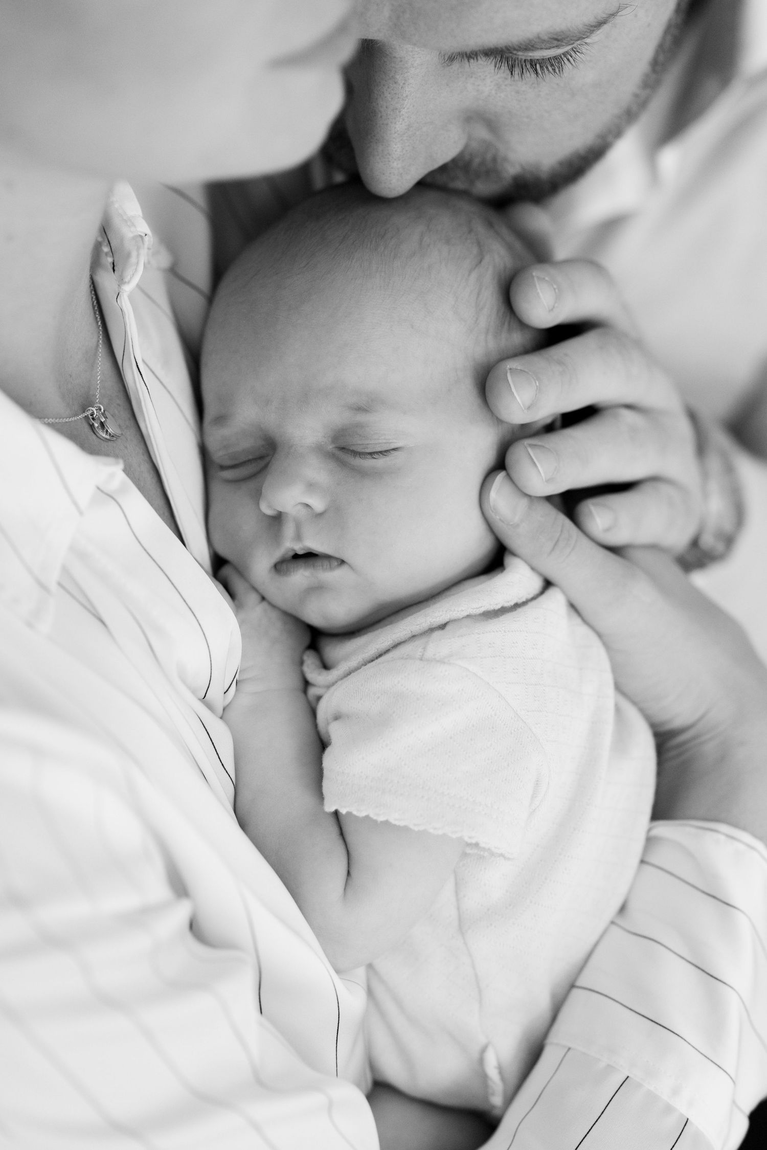 A sleeping newborn baby swaddled in white fabric rests peacefully against soft bedding.