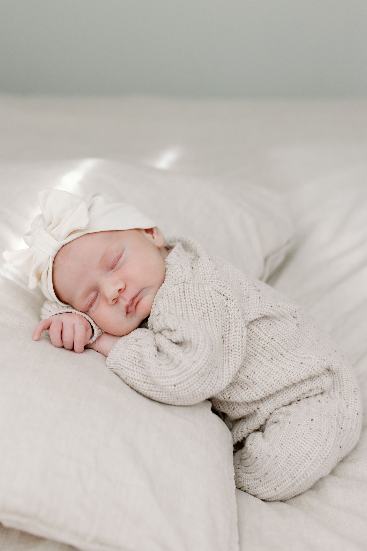 A sleeping baby wearing a cozy white knit sweater lies peacefully on soft white bedding.