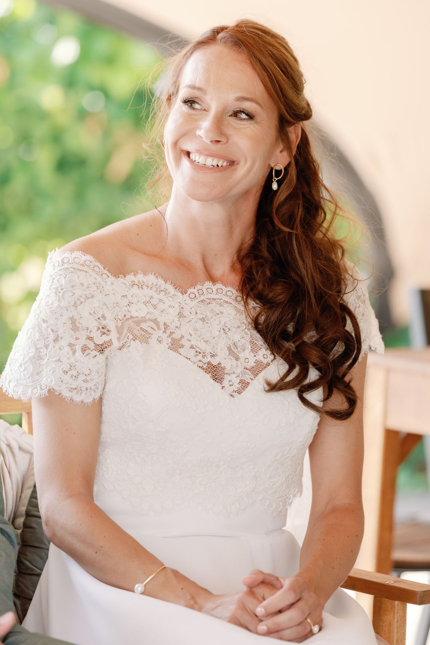 Beautiful bride in white lace off-shoulder wedding dress smiles during outdoor portrait session.