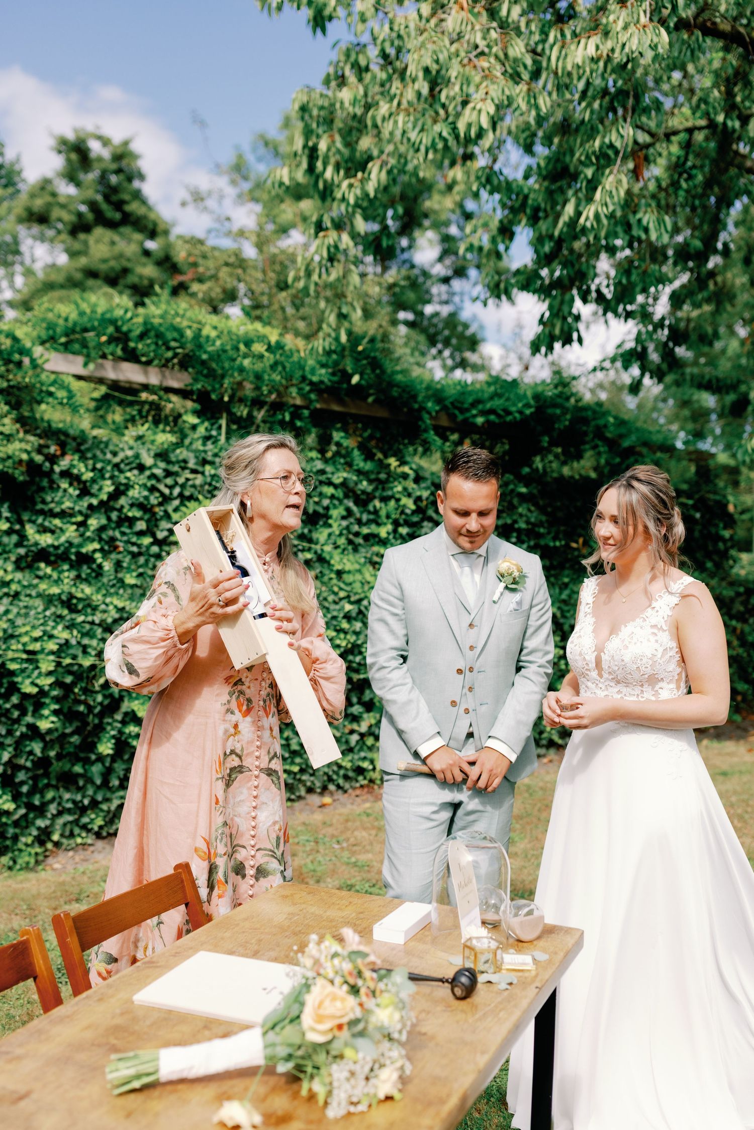 A couple and their wedding party share joyful moments during an outdoor ceremony signing in a garden setting.