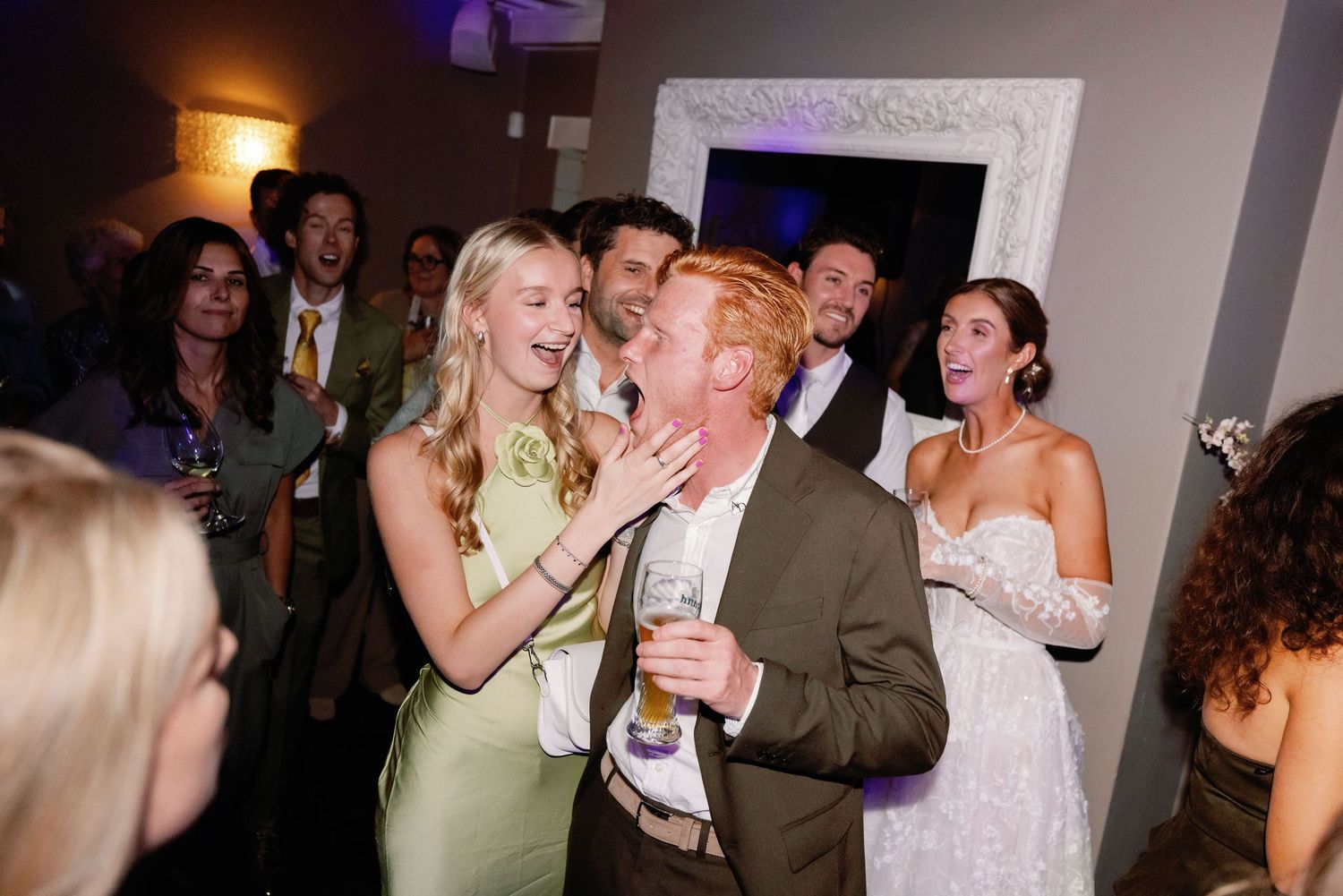 Wedding guests dancing and celebrating together on a dimly lit dance floor at an evening reception.