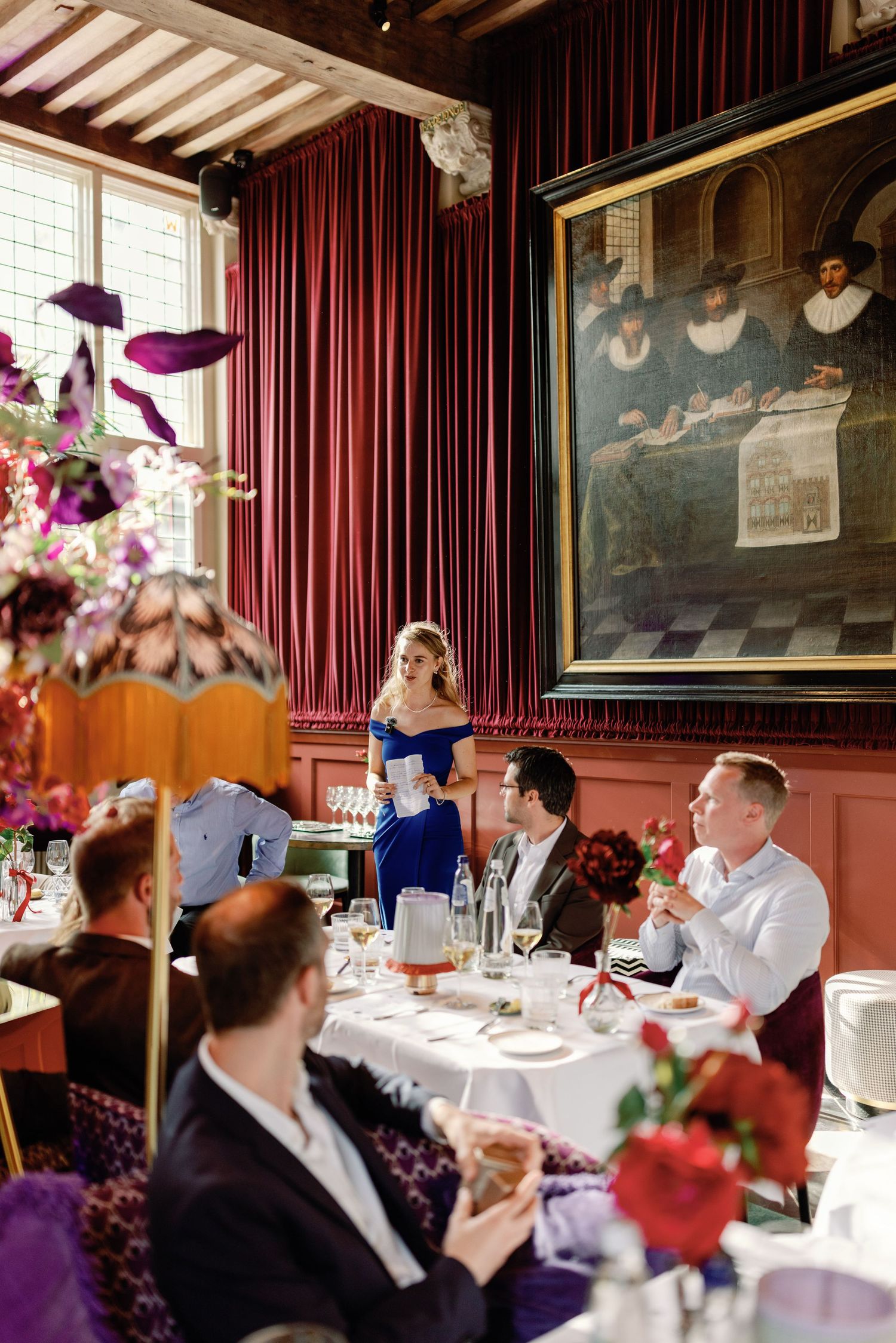 Elegant wedding reception dinner at an upscale restaurant with dark red walls, vintage artwork, and floral centerpieces.
