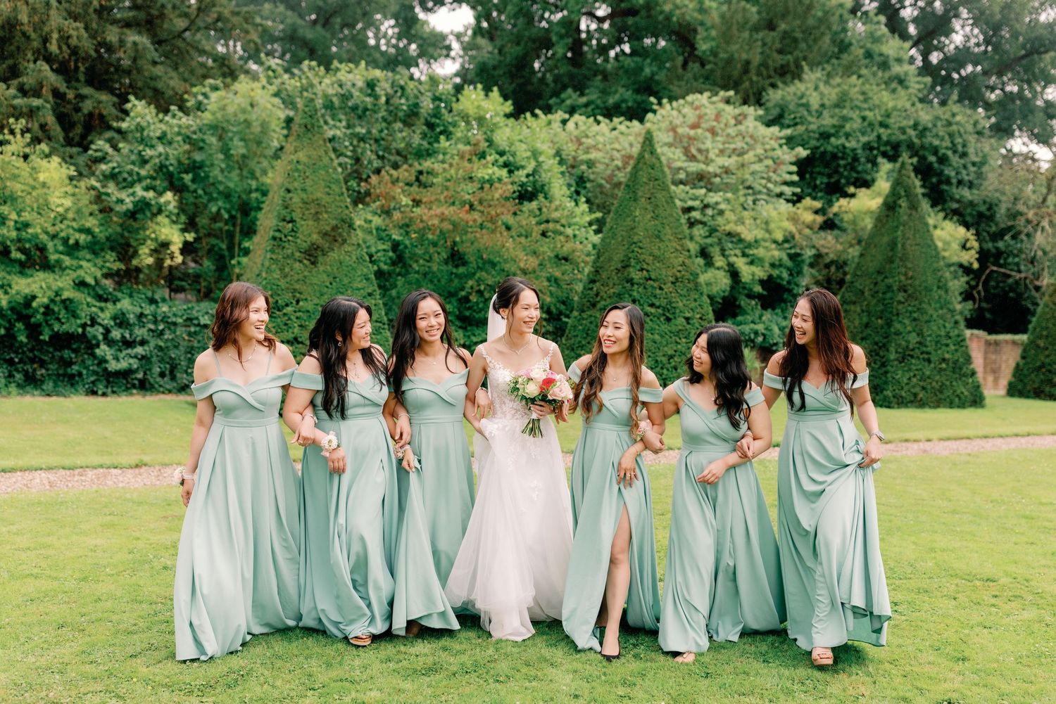 Bridesmaids in light blue dresses walk together on a lush green lawn at an outdoor wedding venue.