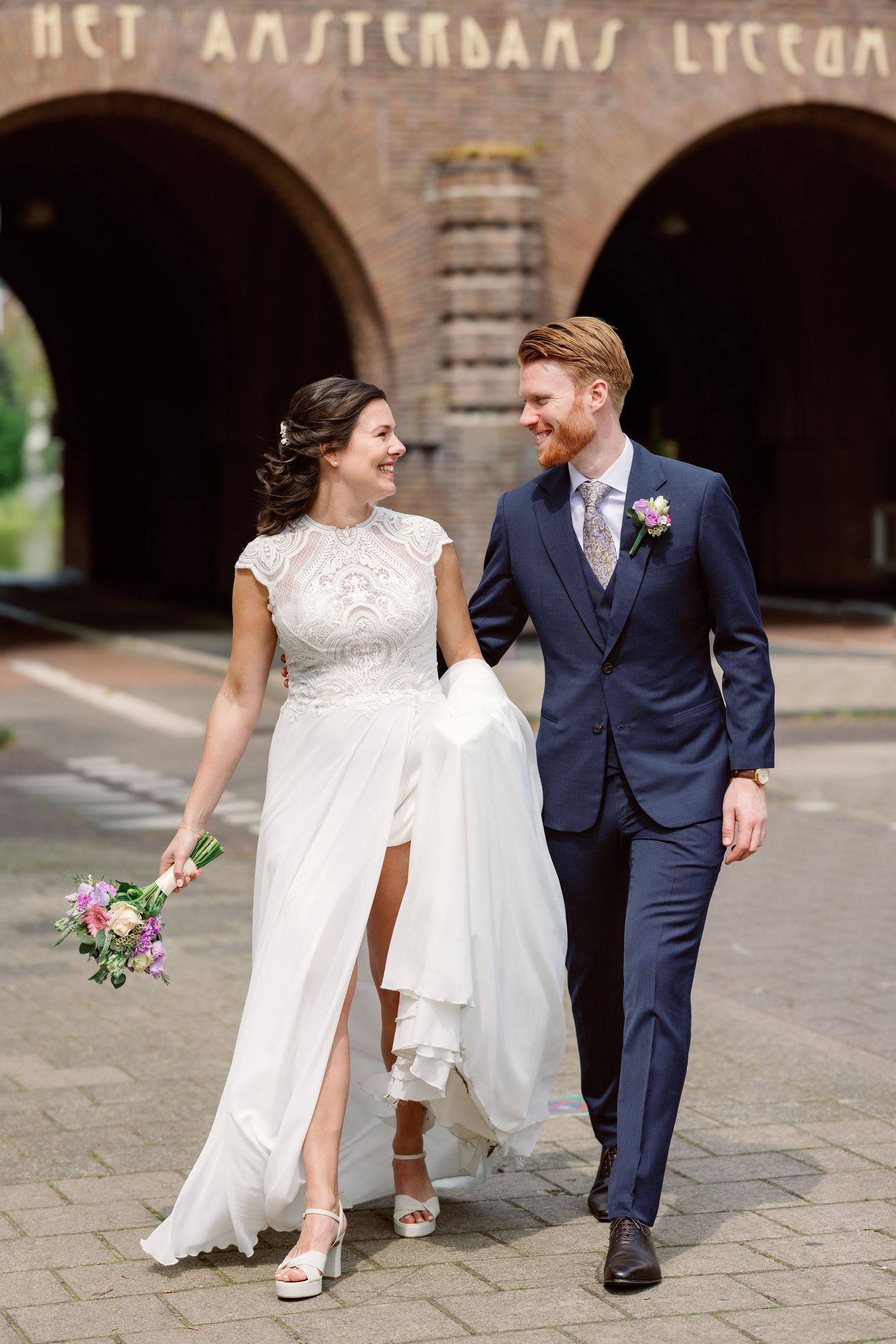Wedding couple walking together on cobblestone pavement near historic brick architecture.