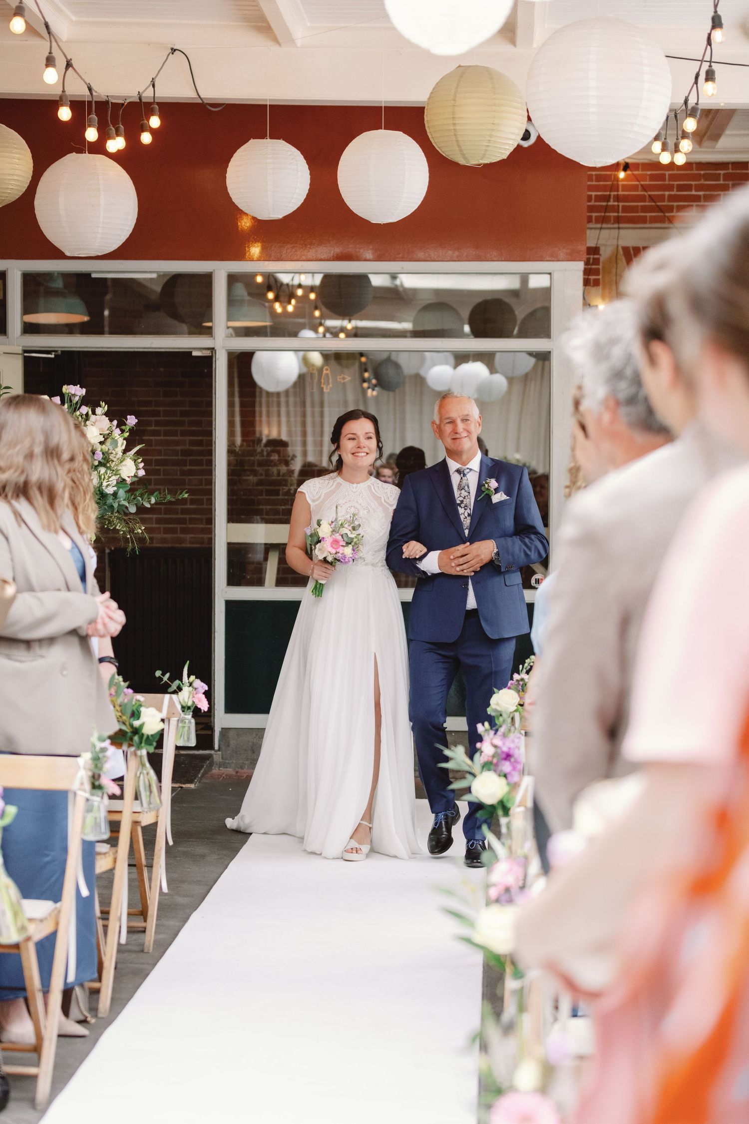 Wedding ceremony in rustic venue decorated with white paper lanterns and floral arrangements.