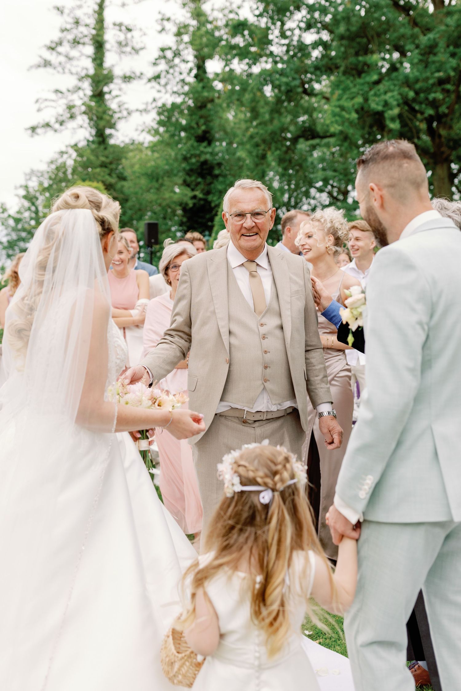 Joyful wedding ceremony outdoors with guests gathered around a bride and groom in a lush garden setting.