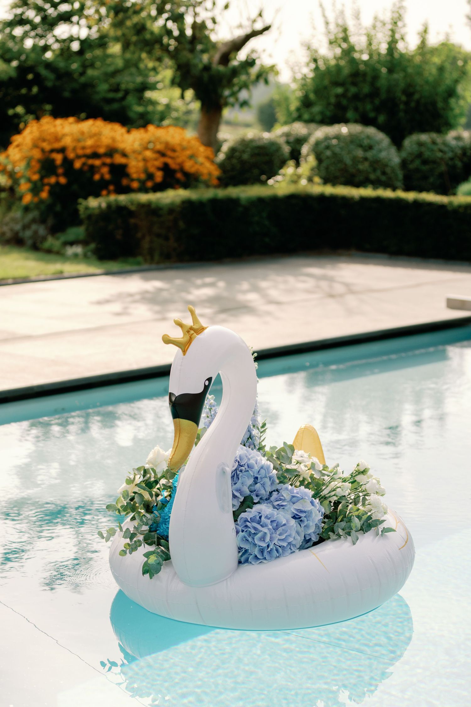 Decorative white swan floats in a pool filled with blue hydrangeas and floral arrangements.