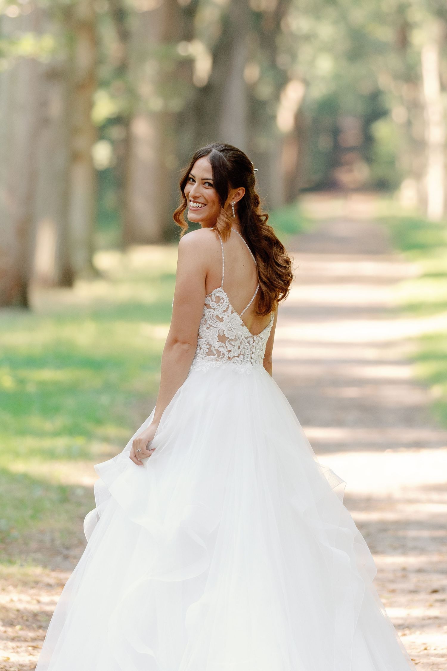 Back view of wedding dress with intricate lace detail on forest path in golden sunlight.
