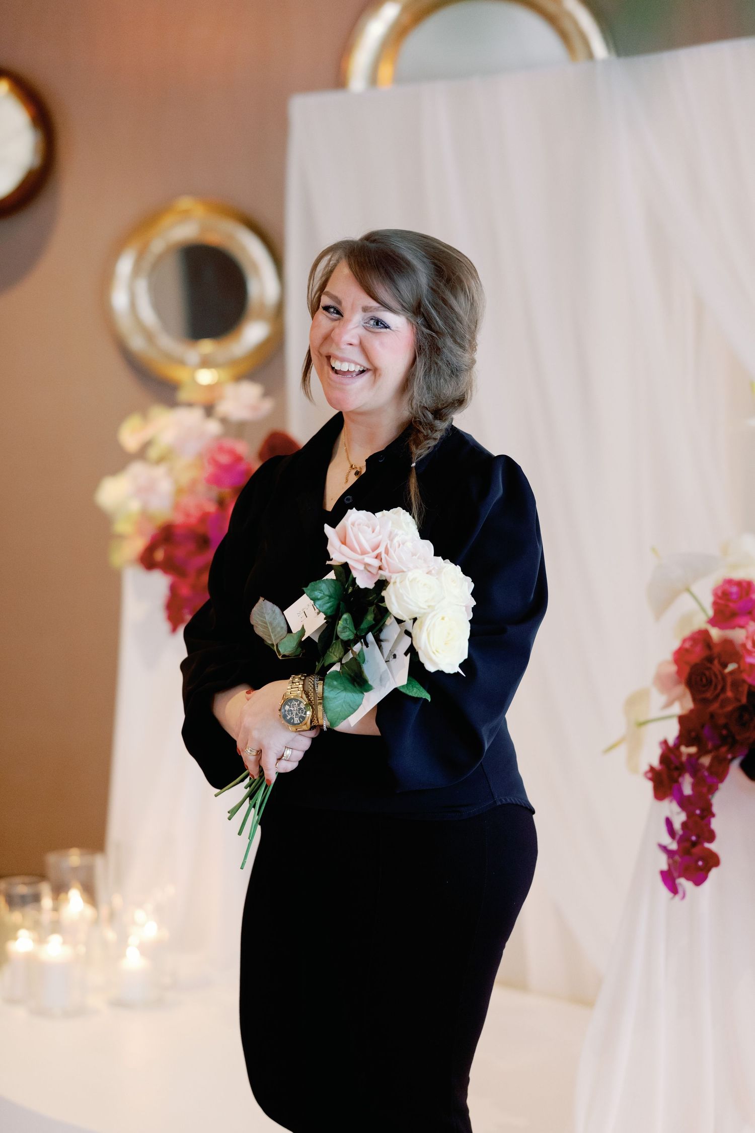 A person in a navy blue blazer holds and smells white flowers while smiling in a warmly lit event space.