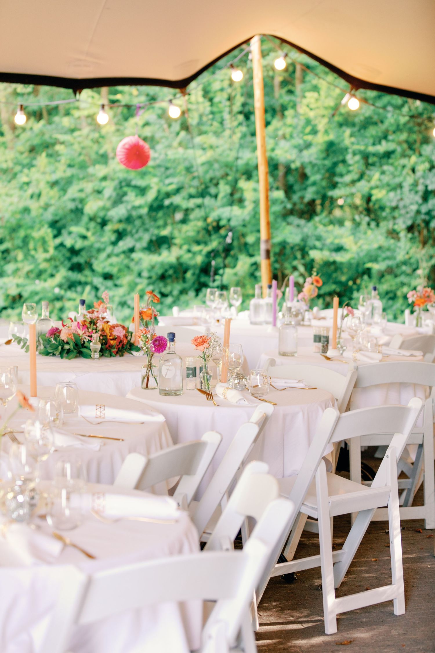 Elegant outdoor wedding reception setup with white tables and chairs under a tent canopy.