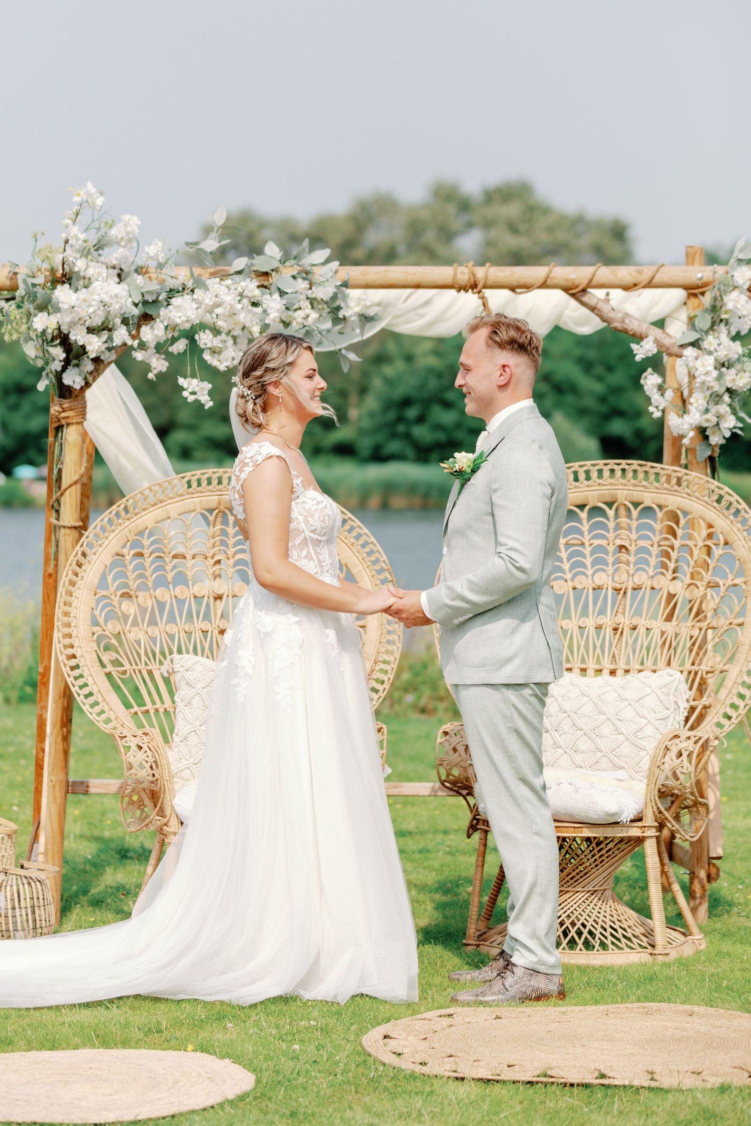 Wedding couple sits together on ornate wicker peacock chairs in an outdoor garden setting.