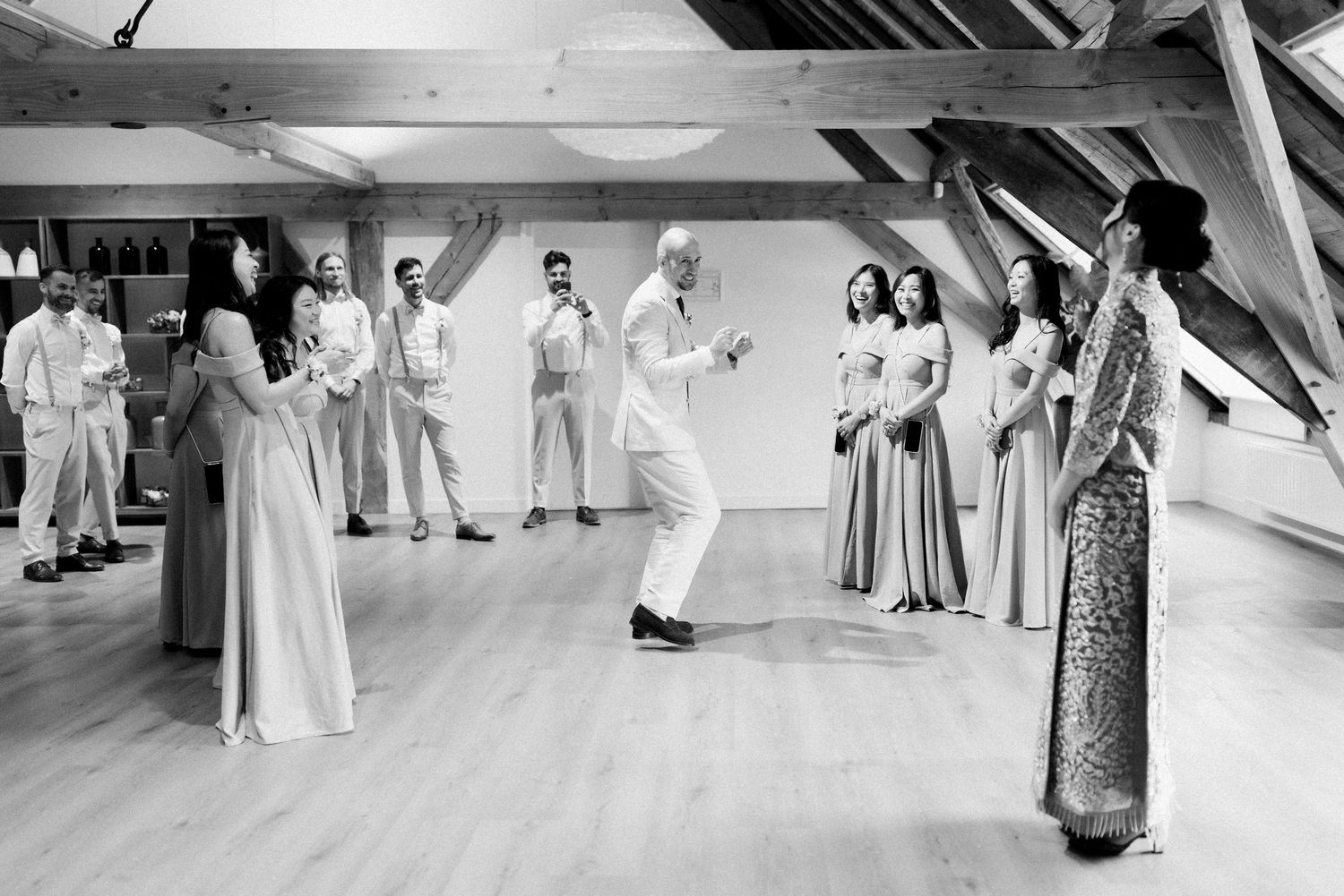 Wedding guests dance together on a wooden floor during a joyful reception celebration.