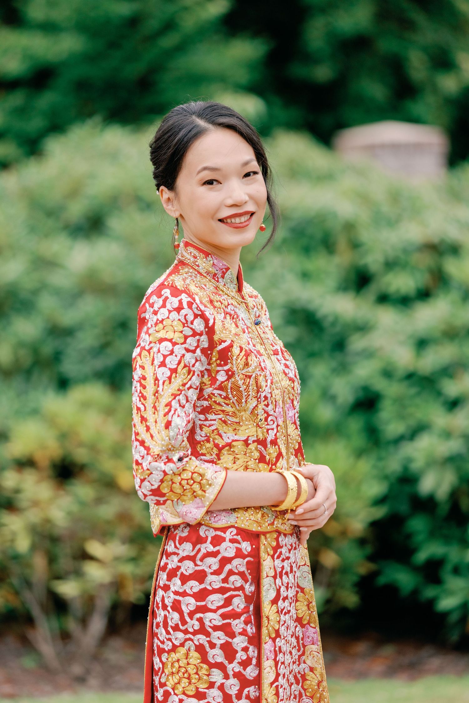 A person wearing a vibrant red and yellow floral dress poses outdoors against a green garden background.