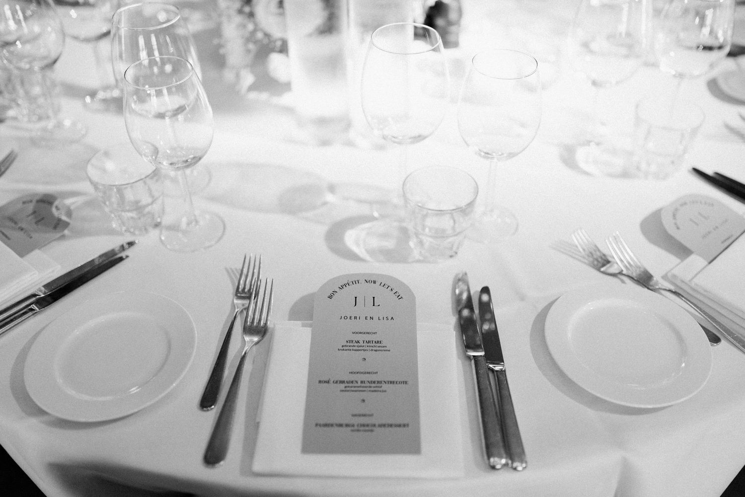 Elegant place settings with white plates, wine glasses, and silverware arranged on a formal dining table.