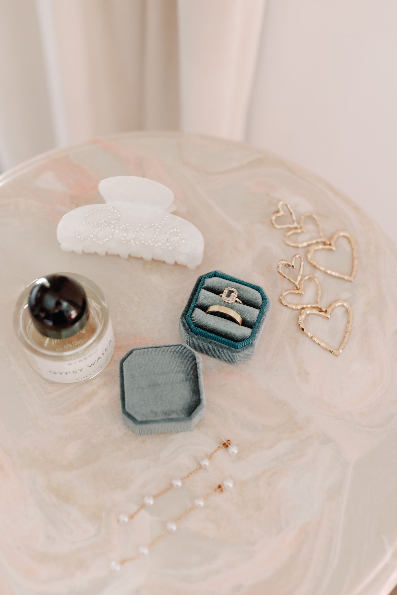 Elegant wedding ring boxes in sage green velvet with gold jewelry and decorative elements on white fabric.