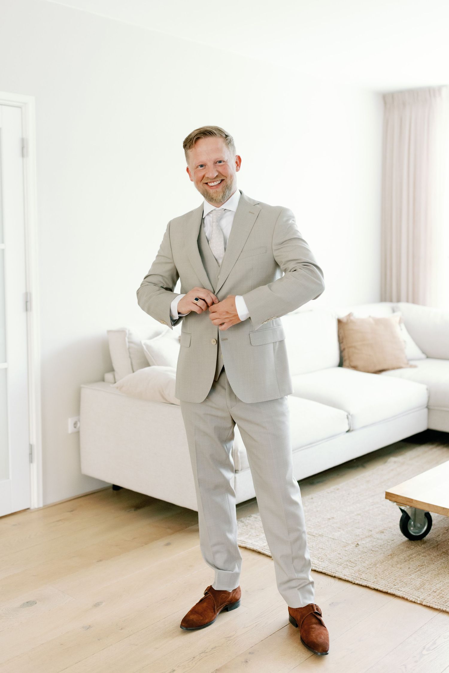 A person in a light gray suit dances and poses playfully in a bright white modern living room interior.