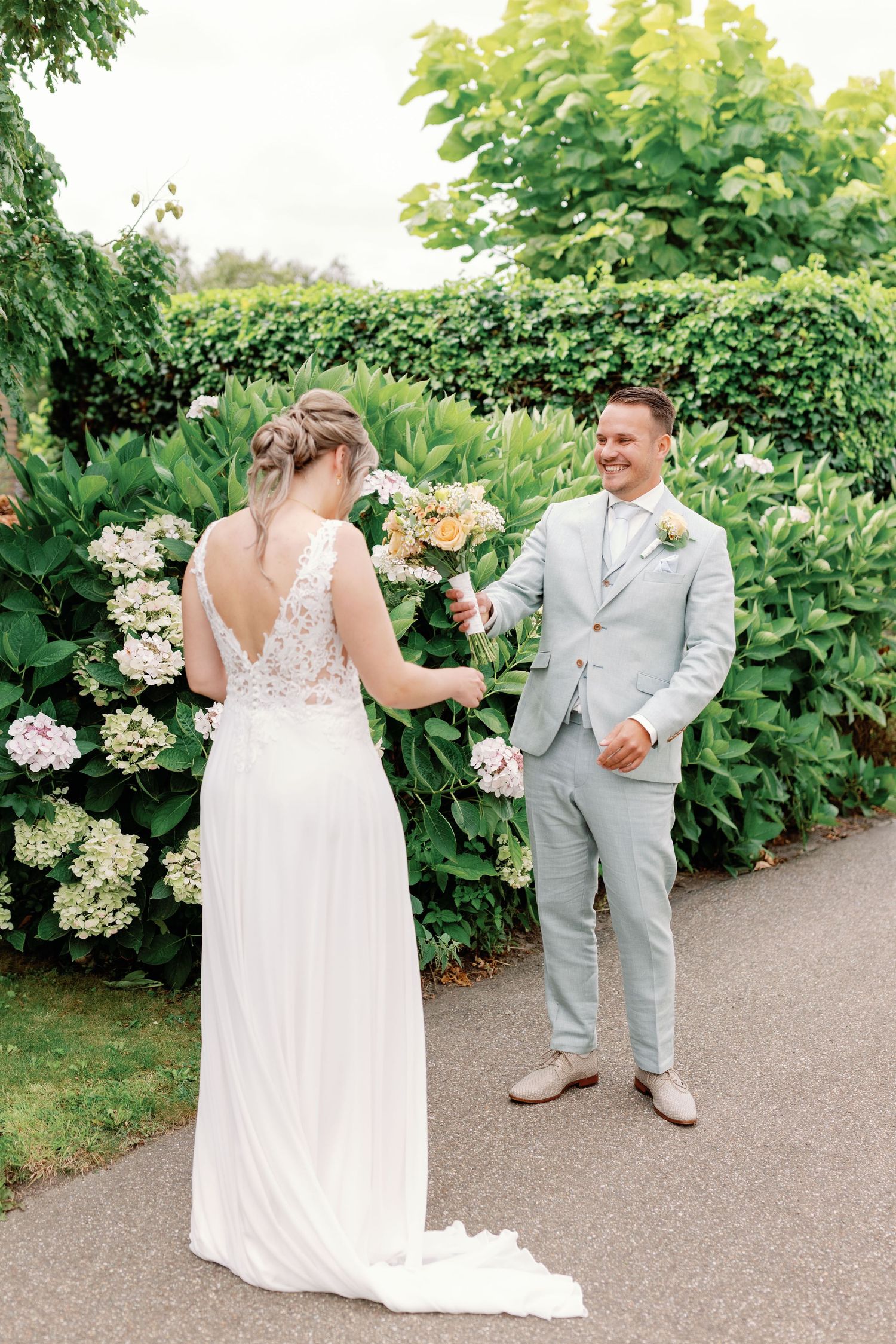 A romantic wedding first look moment captured in a lush garden path with blooming hydrangeas and greenery.