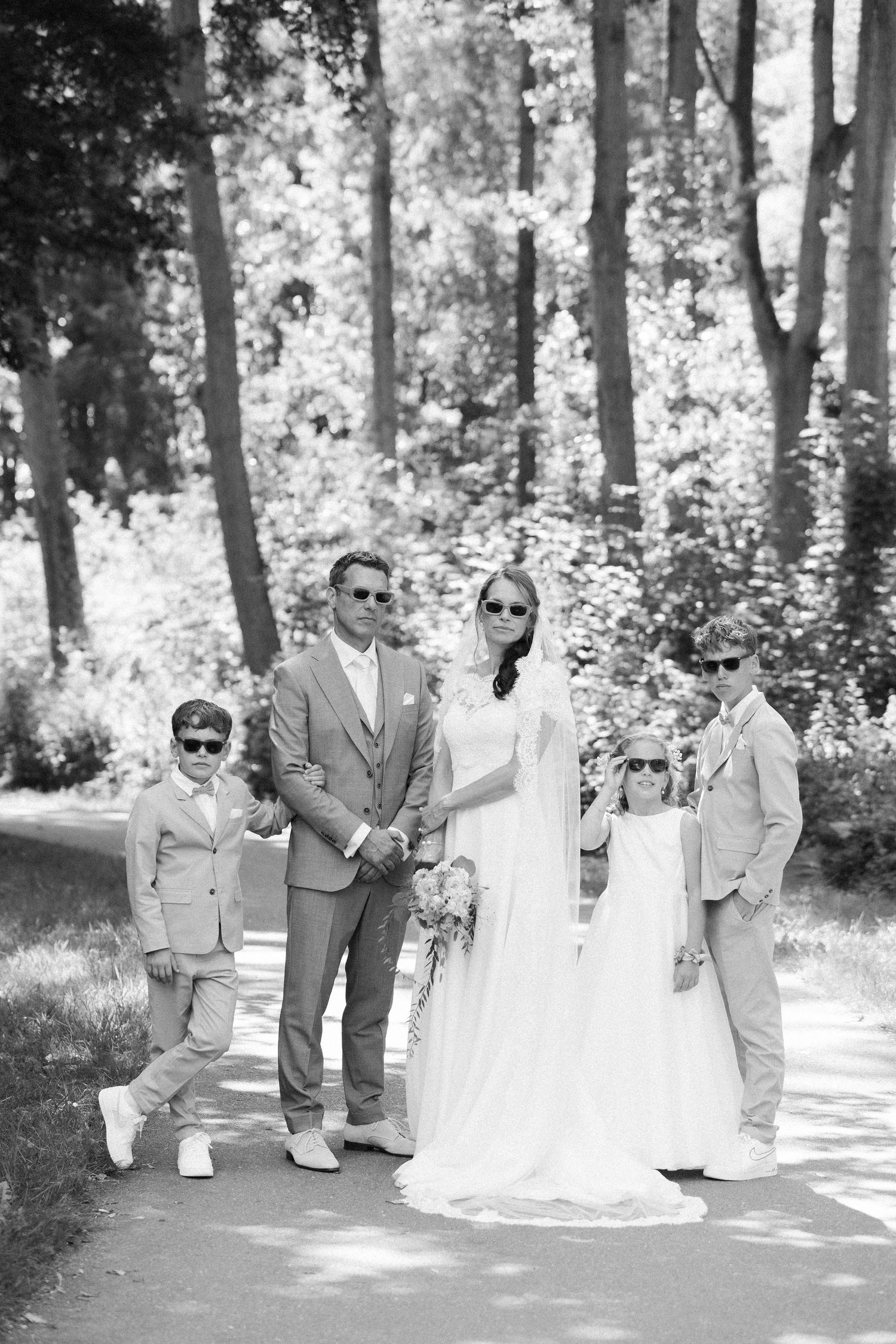 Wedding party poses together in a series of black and white photos along a sunlit wooded path.