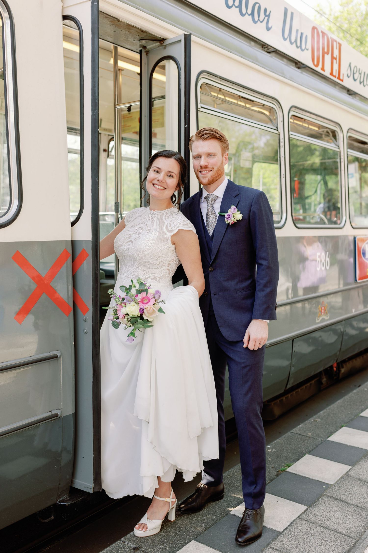 A wedding couple poses for photos beside a train at a transit station platform on their special day.