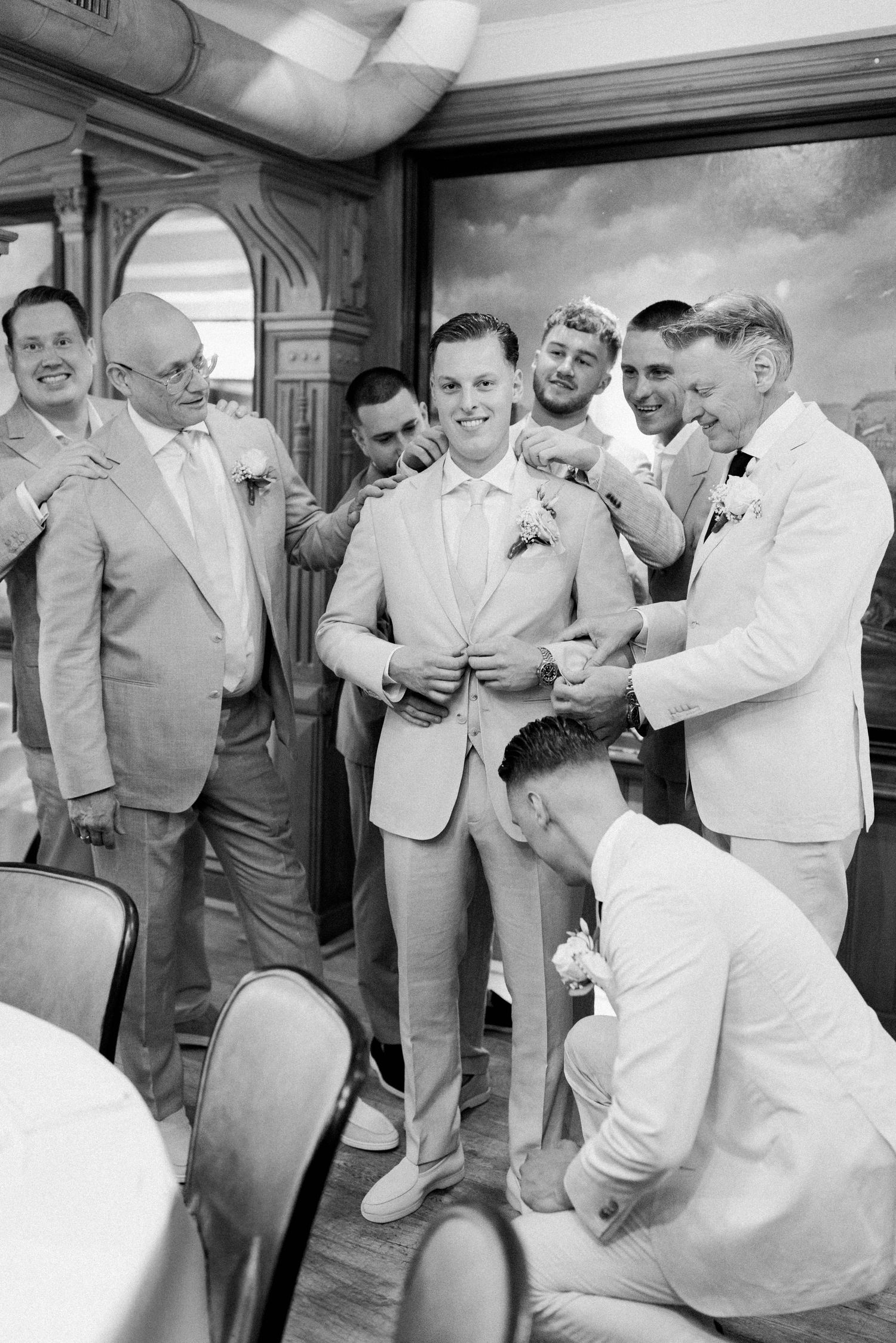 A sequence of black and white photos showing groomsmen laughing and sharing emotional moments at a wedding celebration.