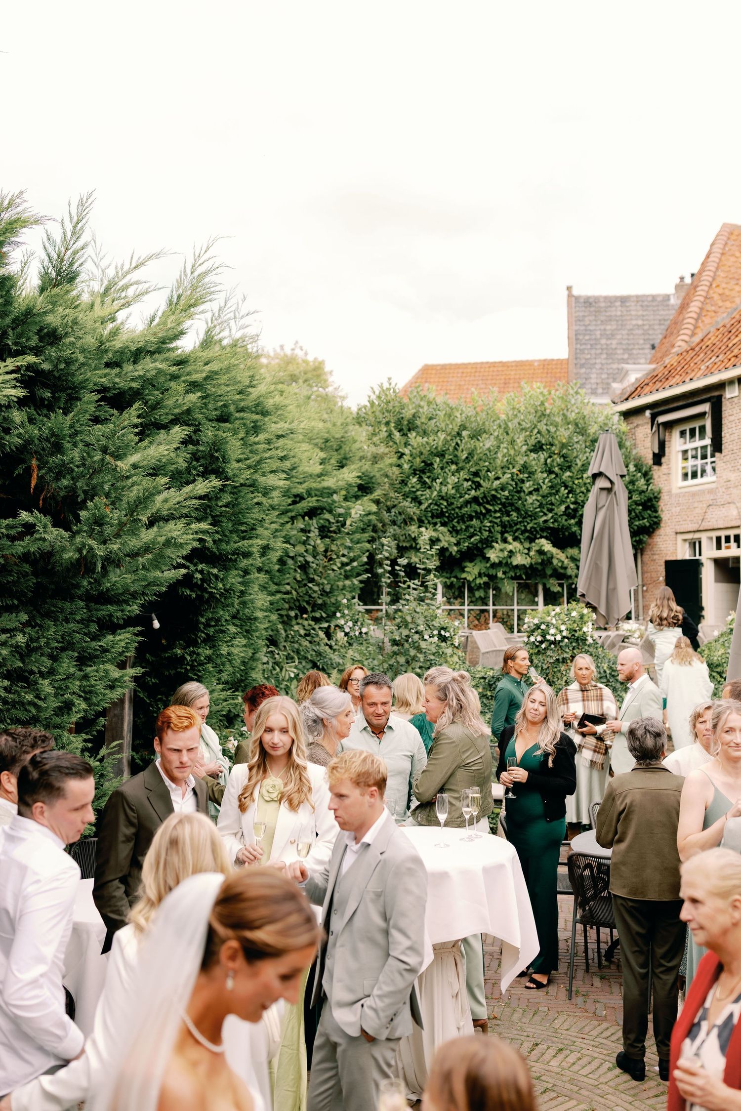 Wedding guests gather in an outdoor courtyard setting during a celebration, surrounded by greenery and traditional buildings.