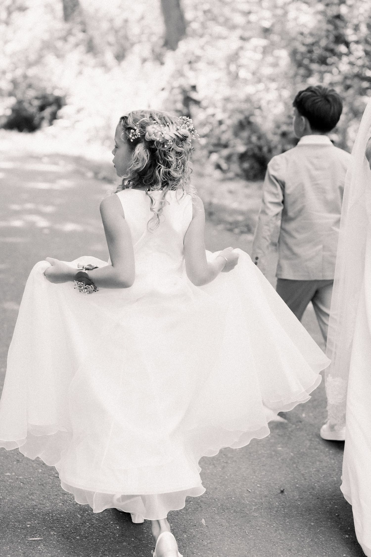 Black and white photo of children in white dresses and formal attire running and playing at an outdoor event.