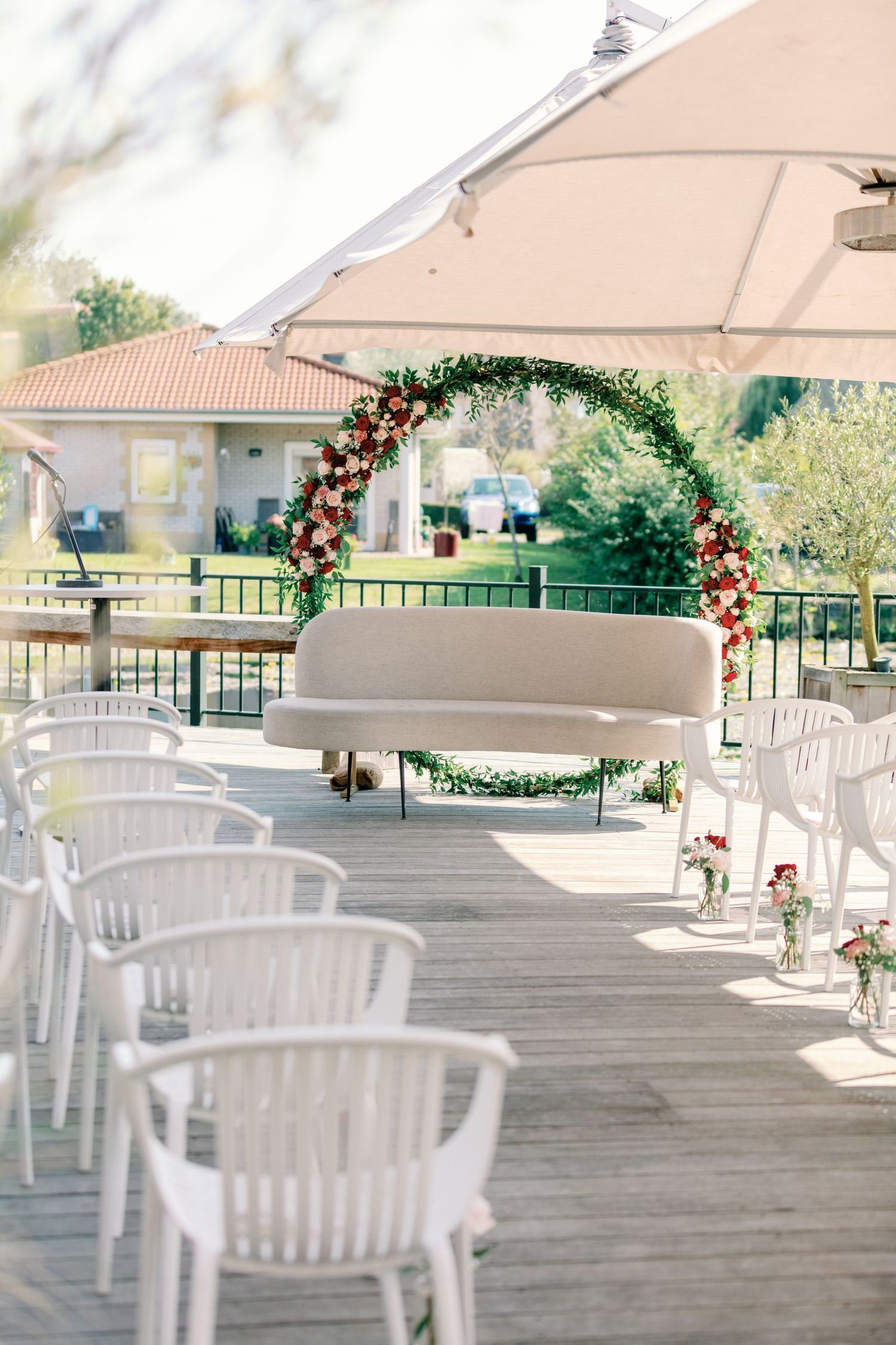 An outdoor wedding ceremony setup with white chairs and a floral arch under a beige canopy.