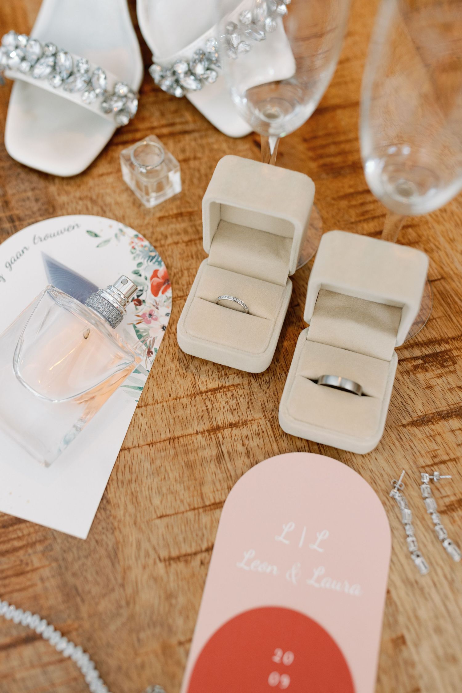 Wedding rings displayed in white boxes alongside delicate pink stationery on wooden surface.