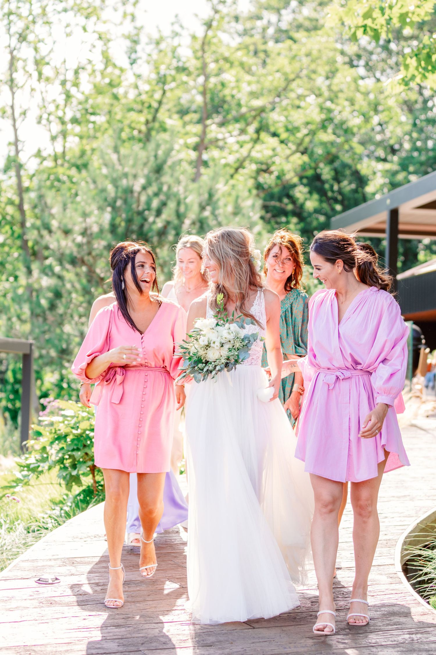 A bridal party walking together on a wooden pathway surrounded by garden scenery.