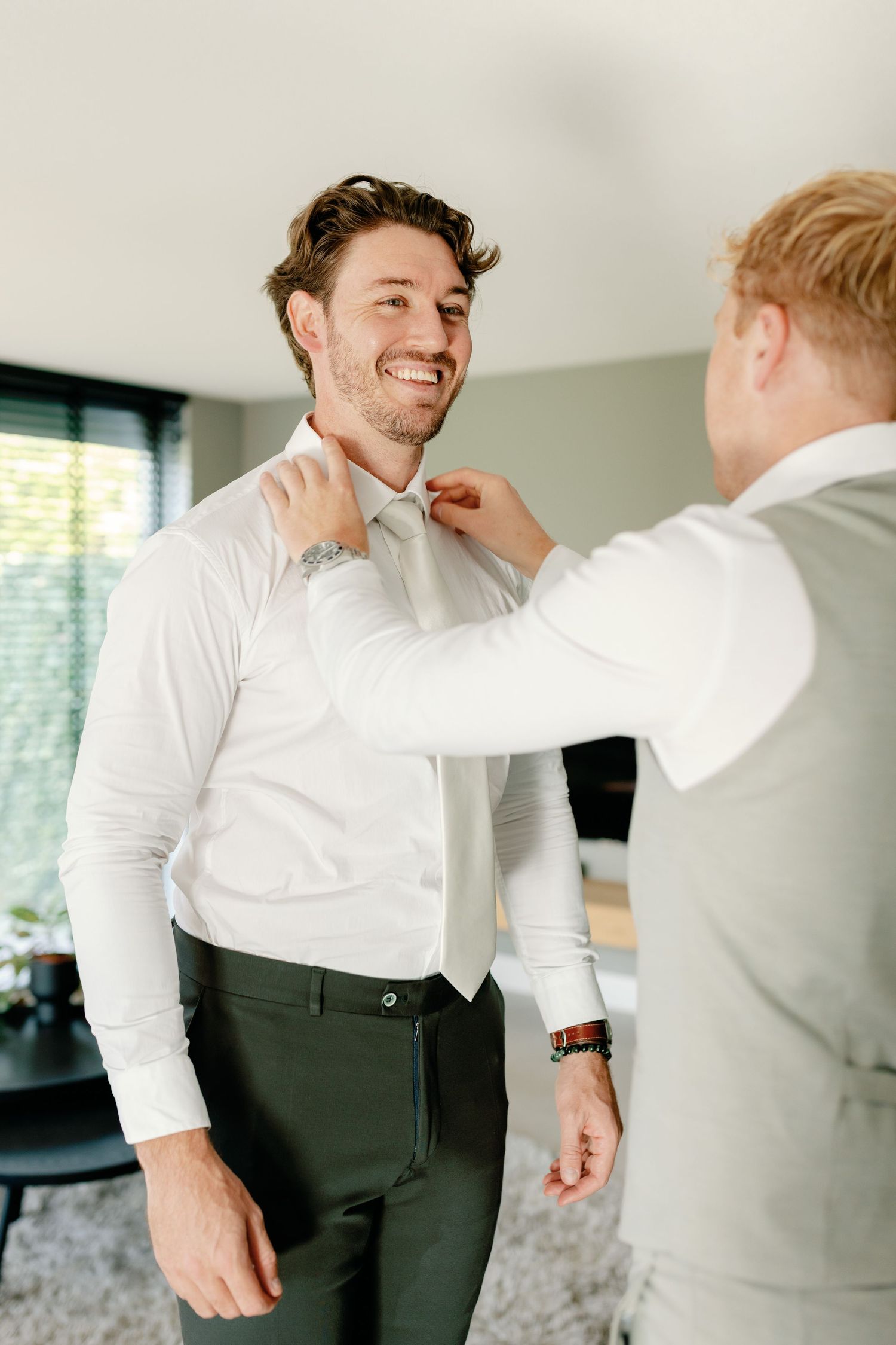 Two people in formal attire share a joyful moment while getting dressed for a special occasion.