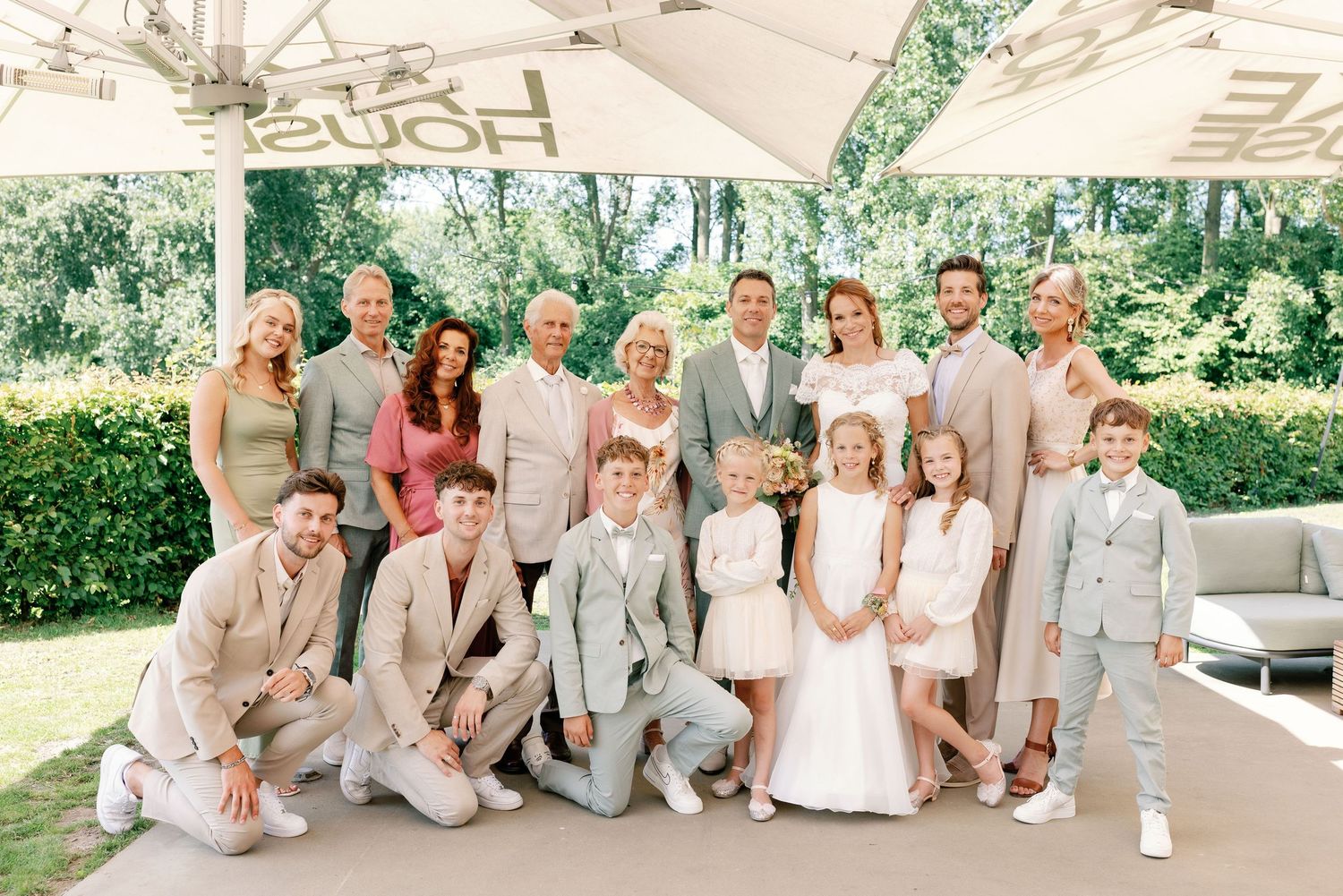 A group in coordinated light gray and white outfits poses together at an outdoor wedding celebration.