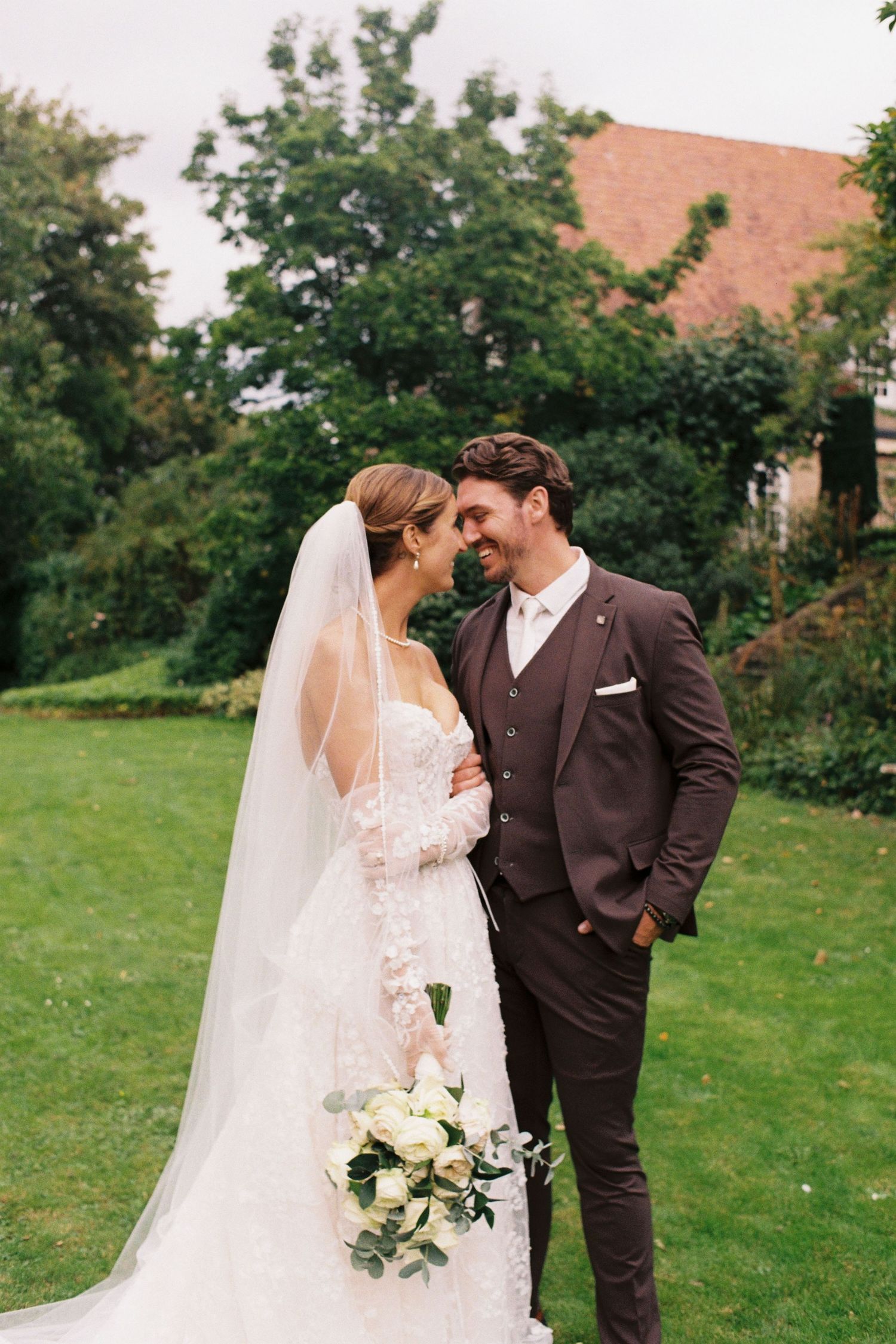 A romantic wedding couple shares intimate moments in a garden setting with lush greenery and white florals.