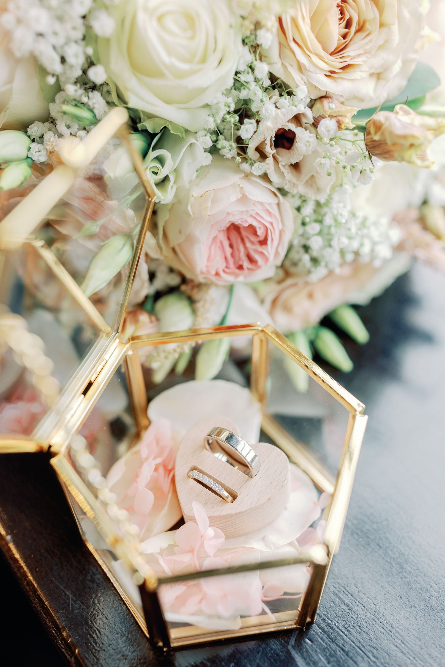 Elegant wedding centerpiece featuring blush pink and white roses with gold geometric accents on a dark surface.