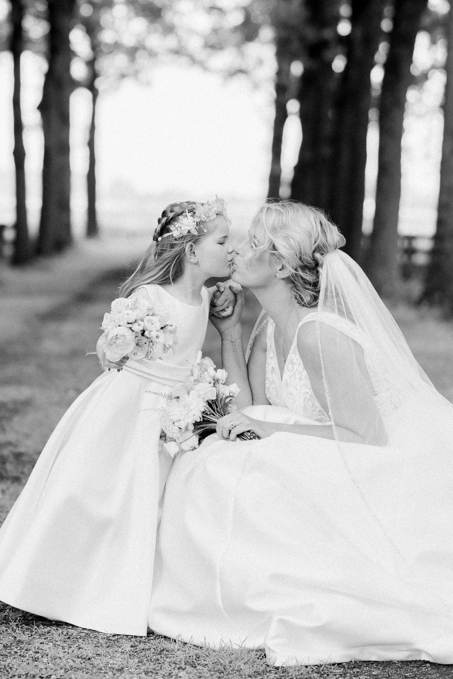 A romantic black and white photo series showing a bride in a flowing white dress resting on grass in a wooded setting.