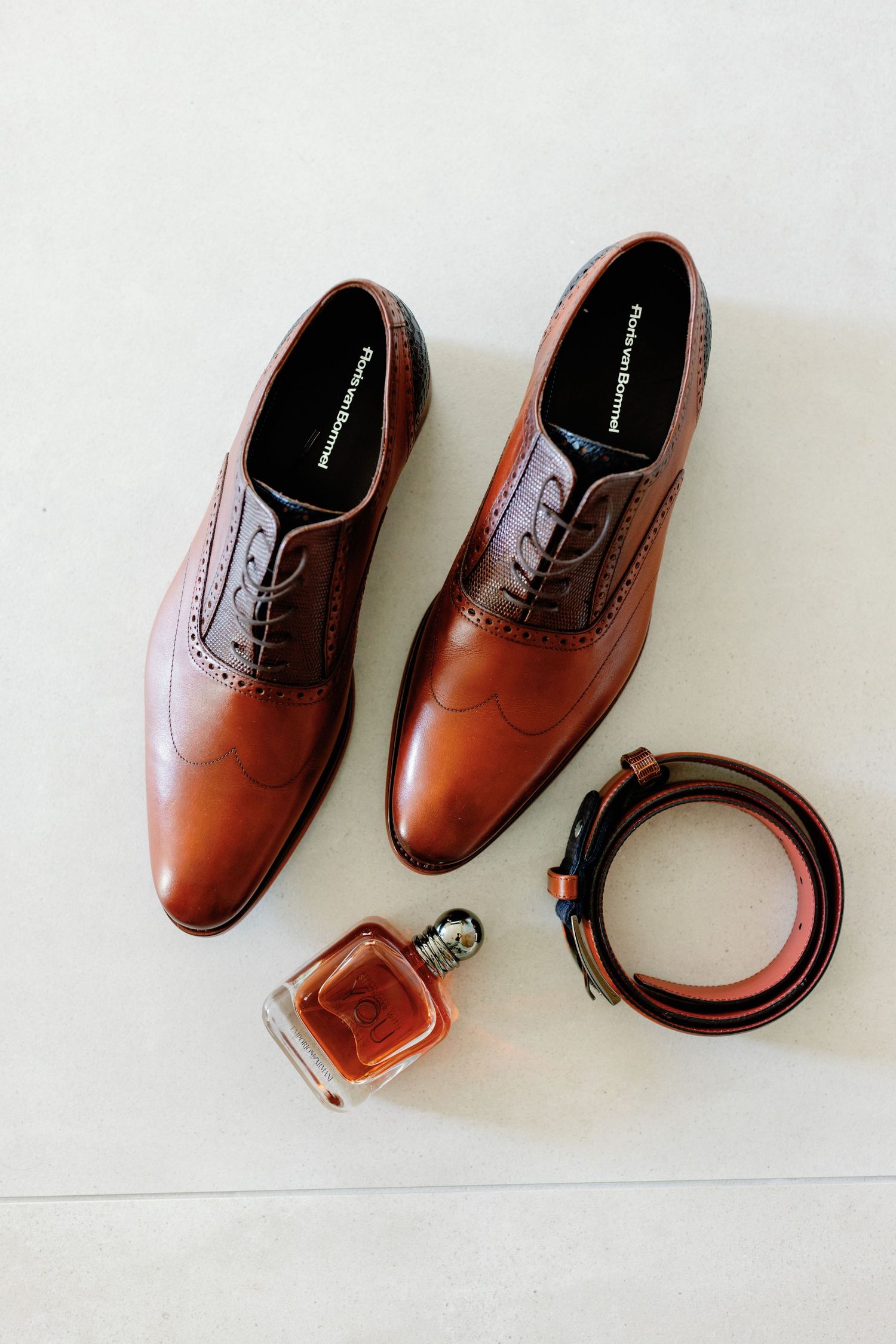 Brown leather oxford dress shoes with matching belt arranged on white background in minimalist style.