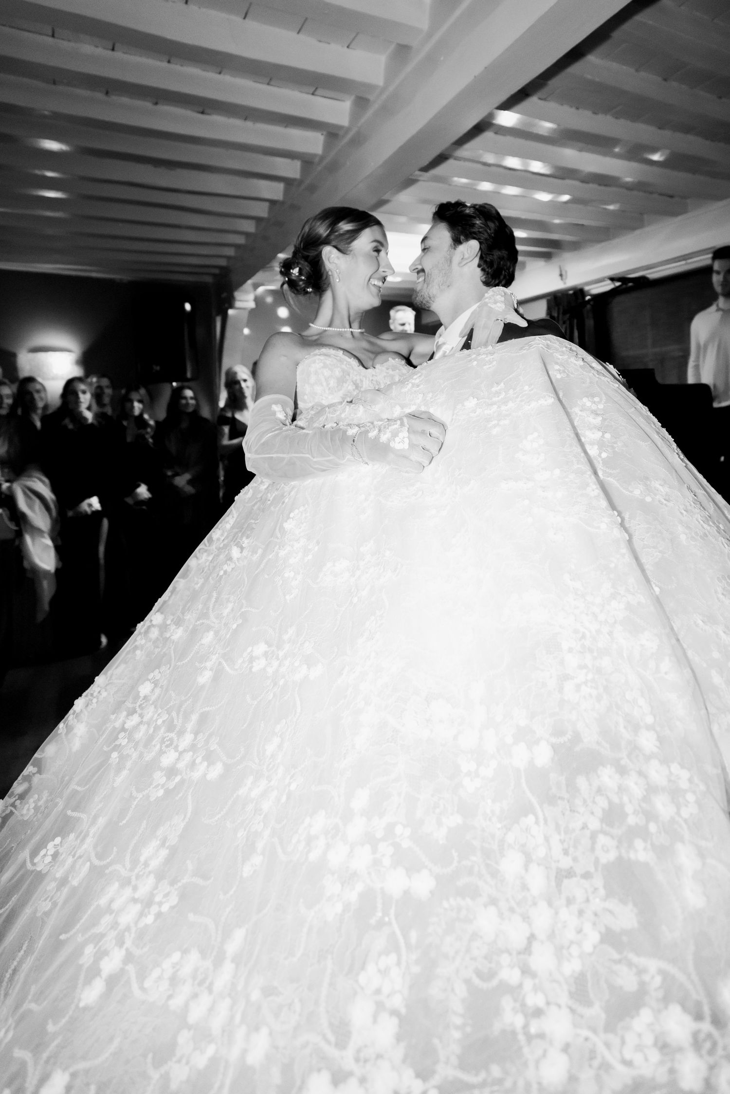 Two people in elegant white wedding attire share an intimate moment during their celebration.