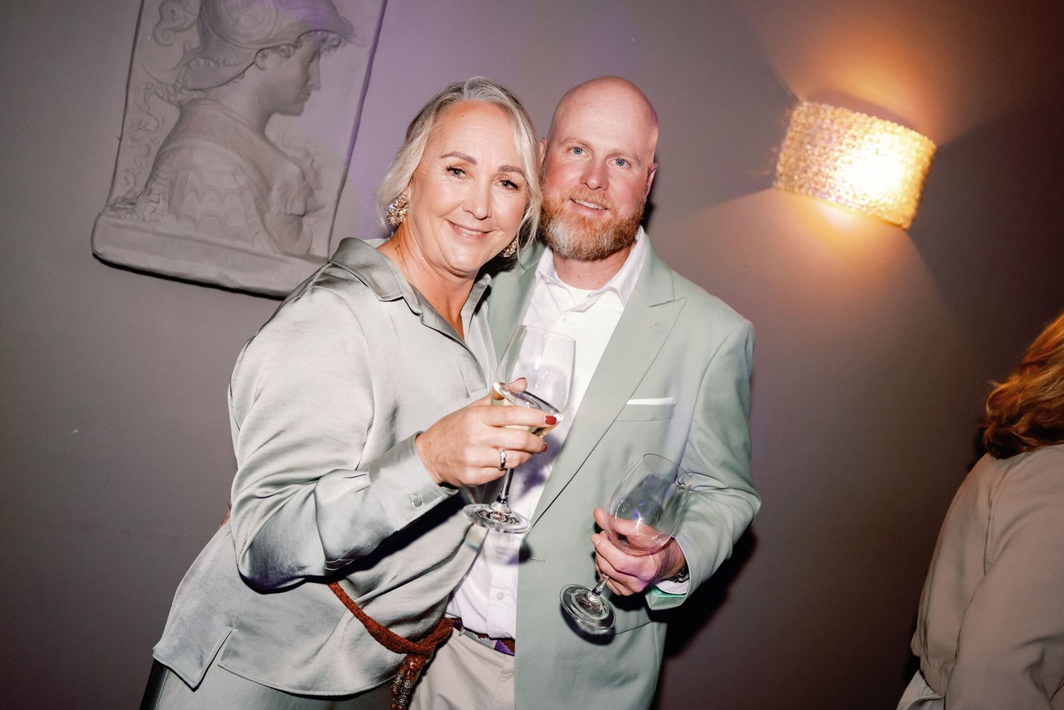People in formal attire smile and raise glasses during a celebratory toast at an indoor event.
