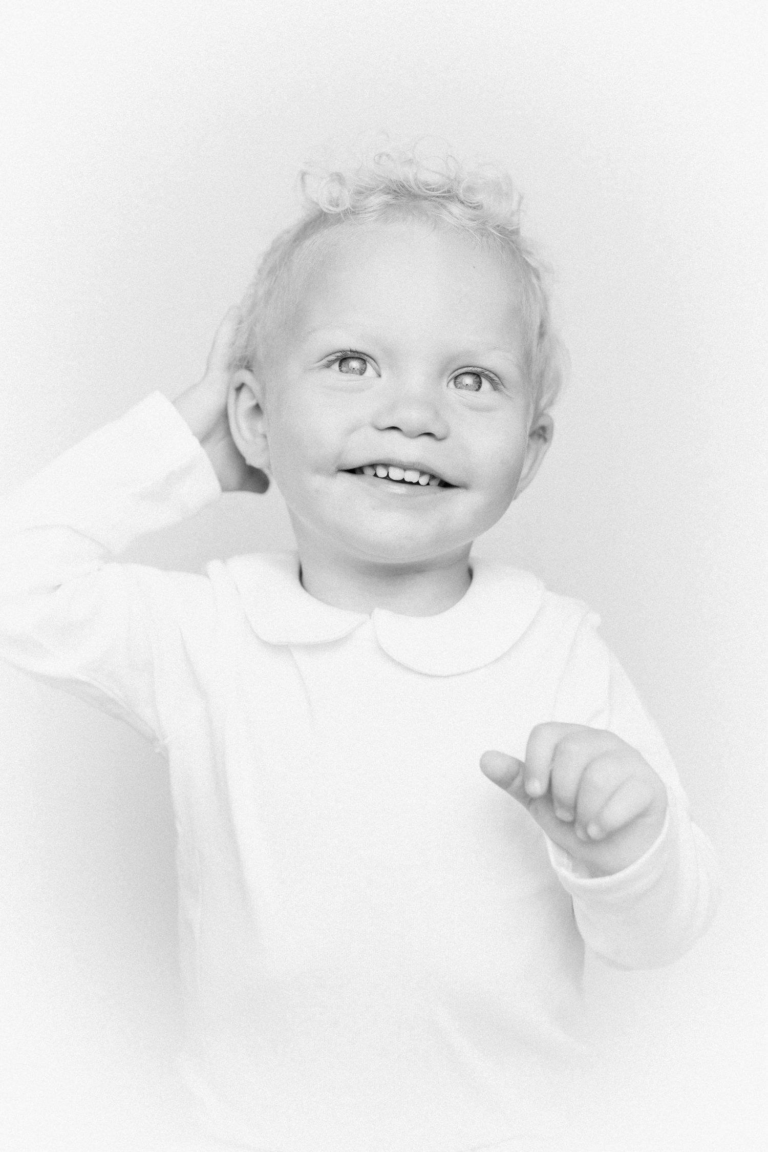 High key portrait of a young child in white clothing against bright background.