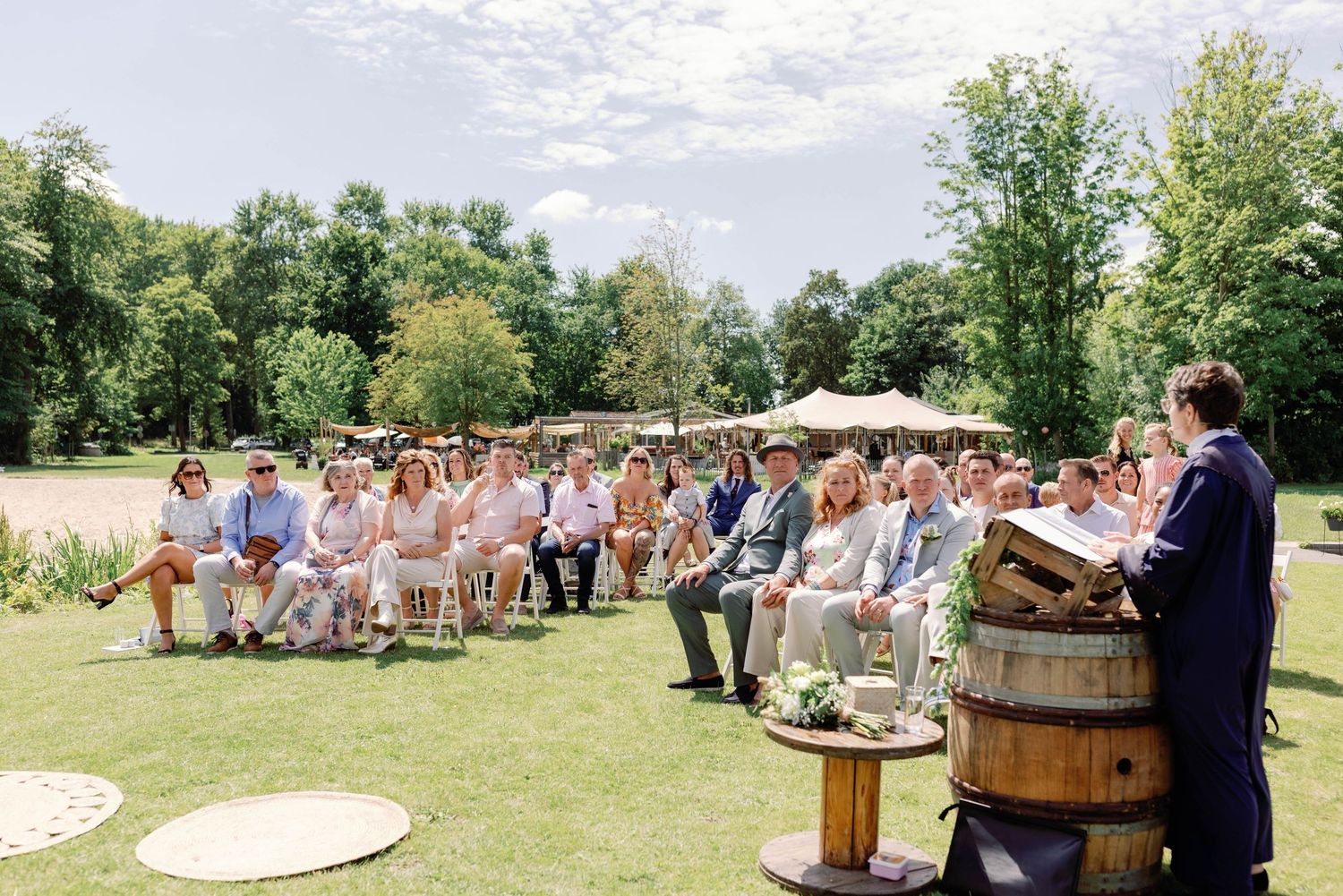 An outdoor wedding ceremony setup with wooden barrels and white chairs arranged on a grassy lawn under blue skies.