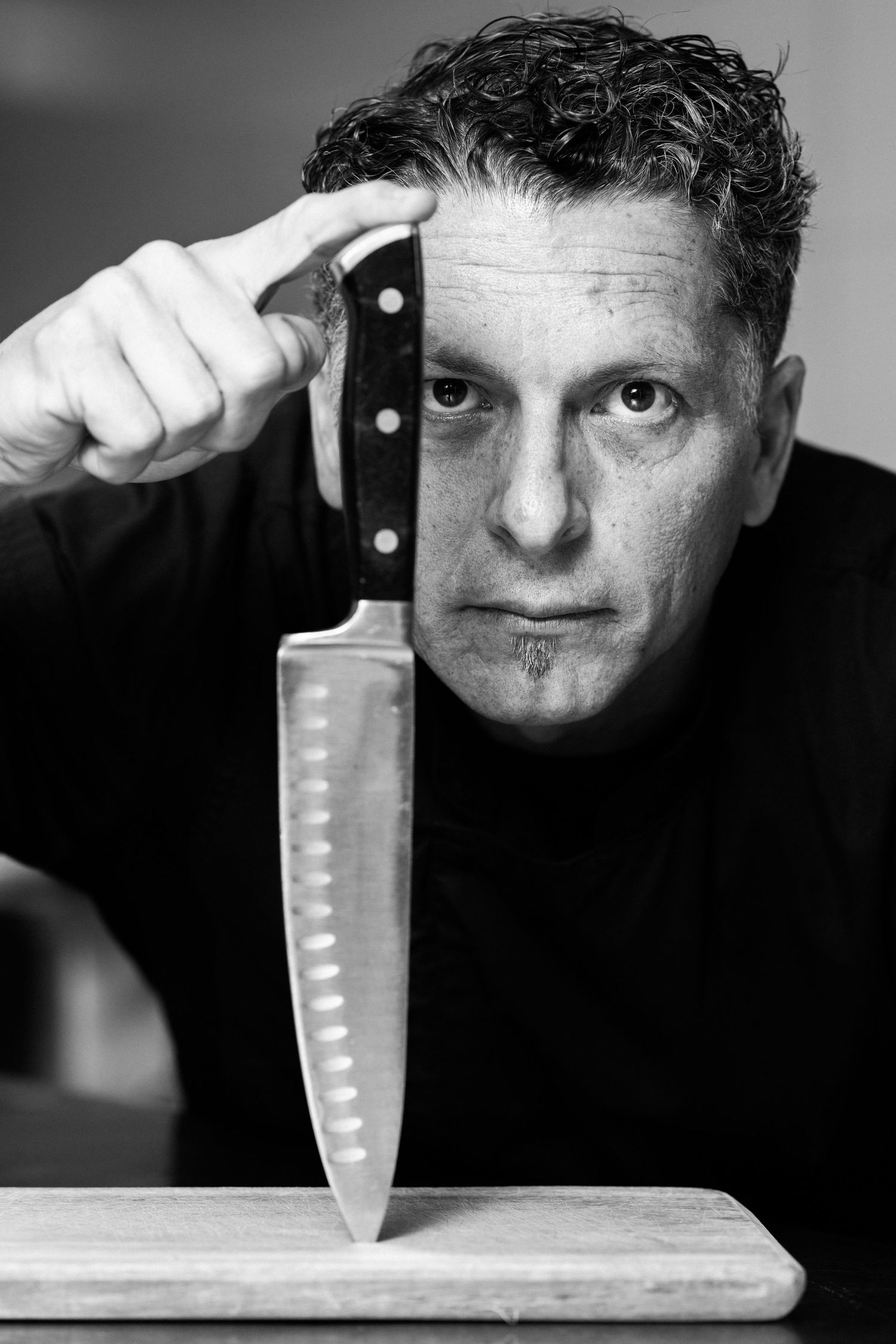 Black and white sequence showing a chef's knife being chopped against a wooden cutting board in dramatic lighting.
