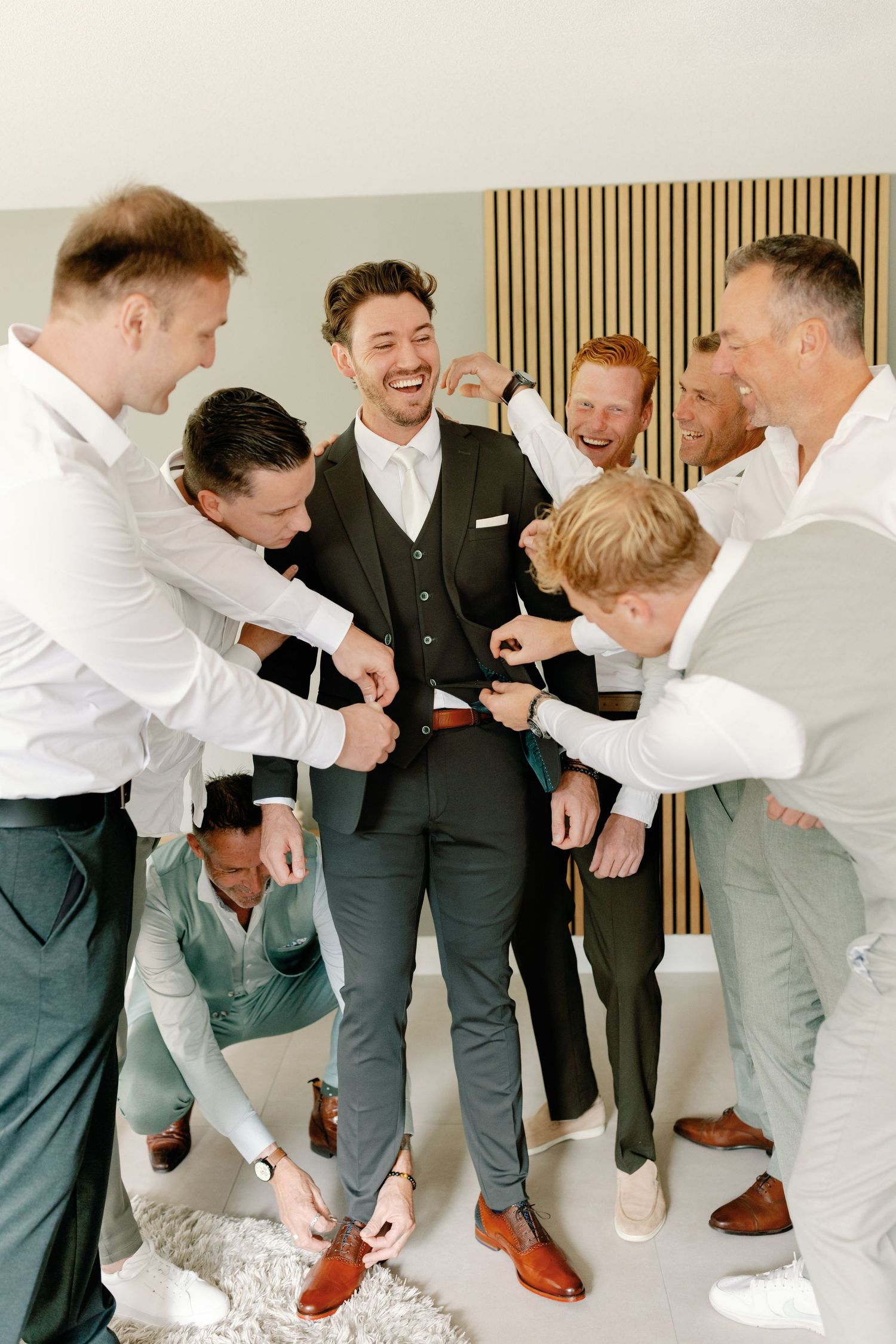 Groomsmen in matching gray suits and white shirts playfully interact during a candid wedding photo session.