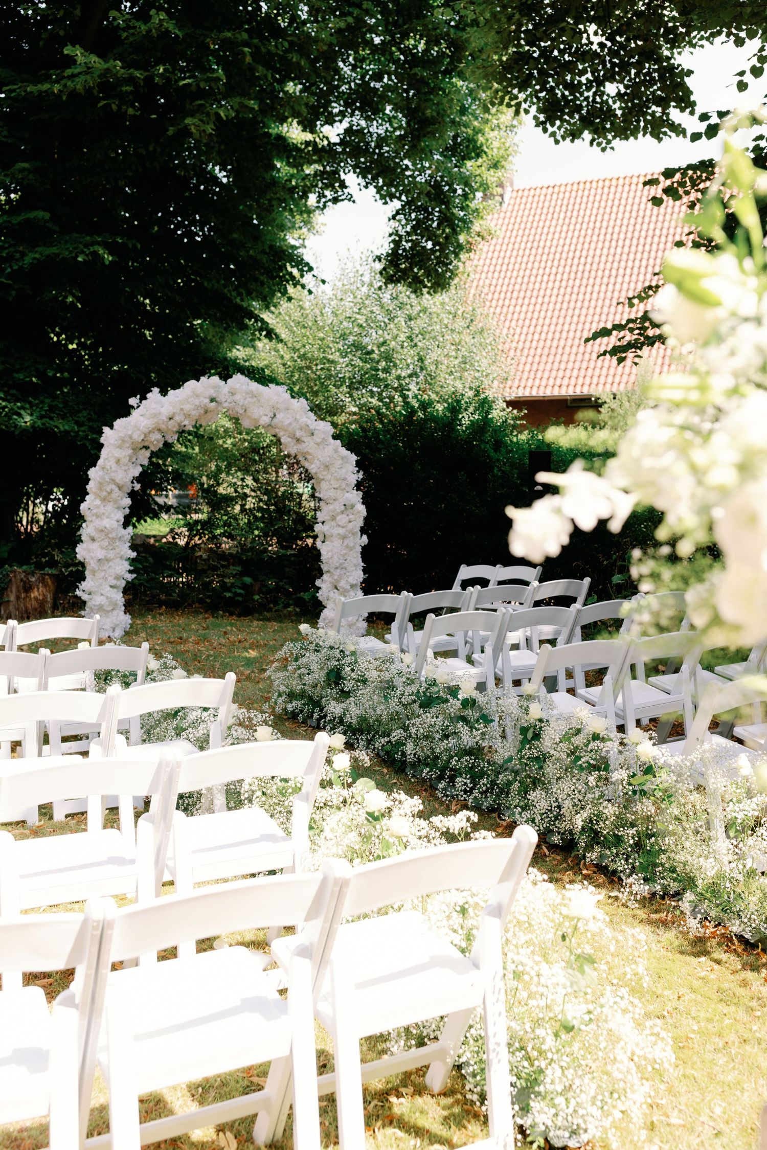 White folding chairs arranged in rows beneath a floral balloon arch for an outdoor garden wedding ceremony.